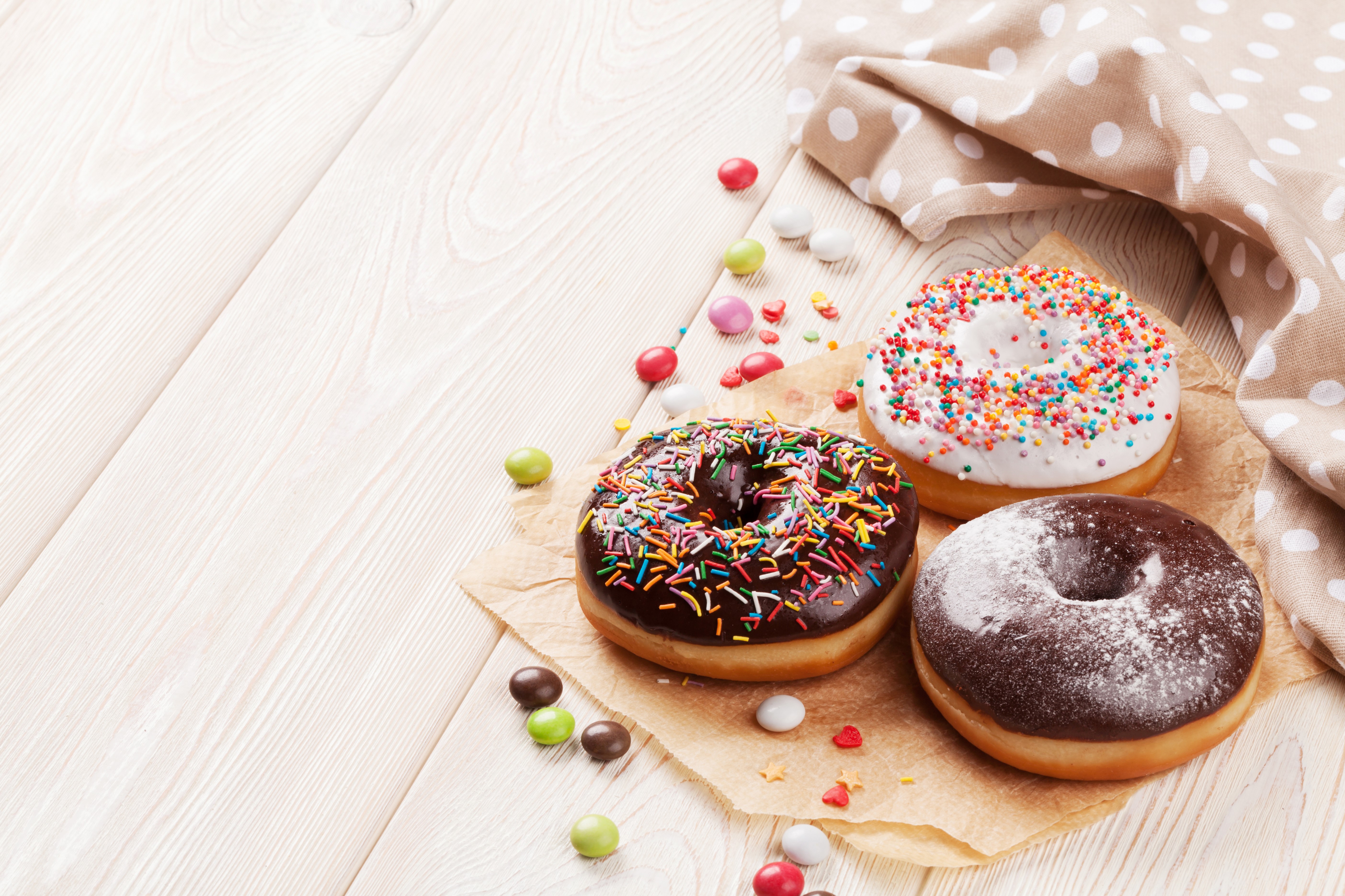 Three donuts with sprinkles and chocolate on wood planks HD Wallpaper