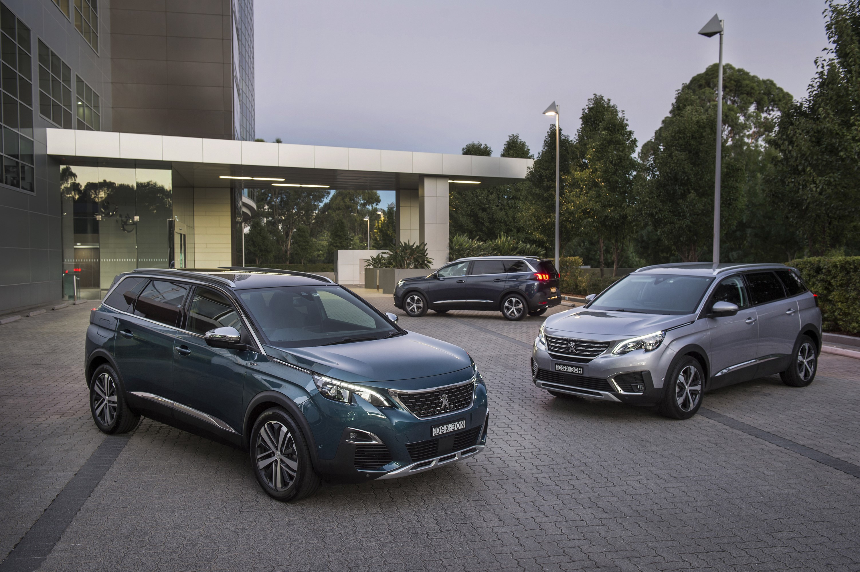 Three Peugeot 5008 SUVs parked outside a modern building HD Wallpaper