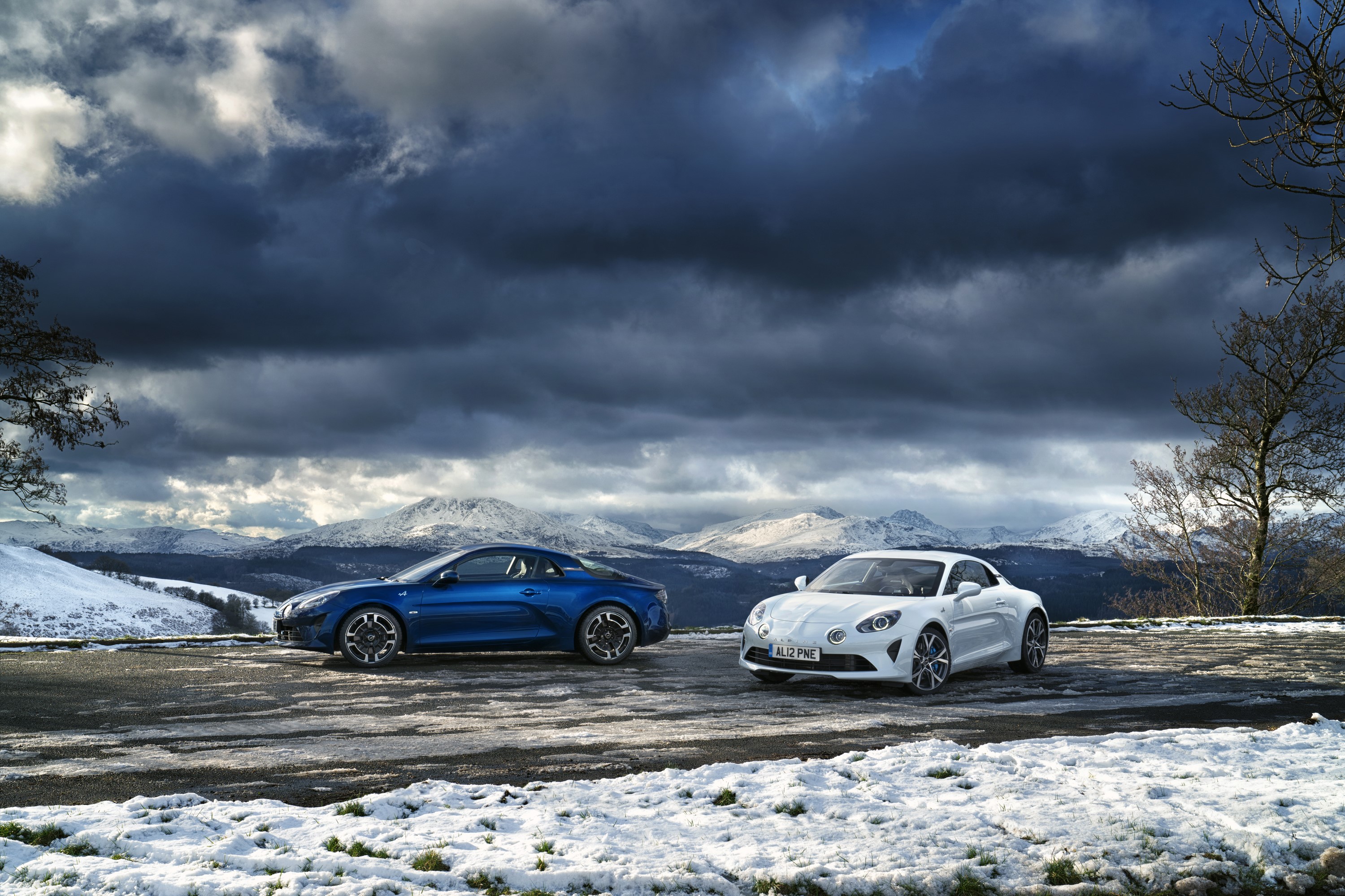 Two Alpine A110 sports cars in a snowy mountain landscape HD Wallpaper