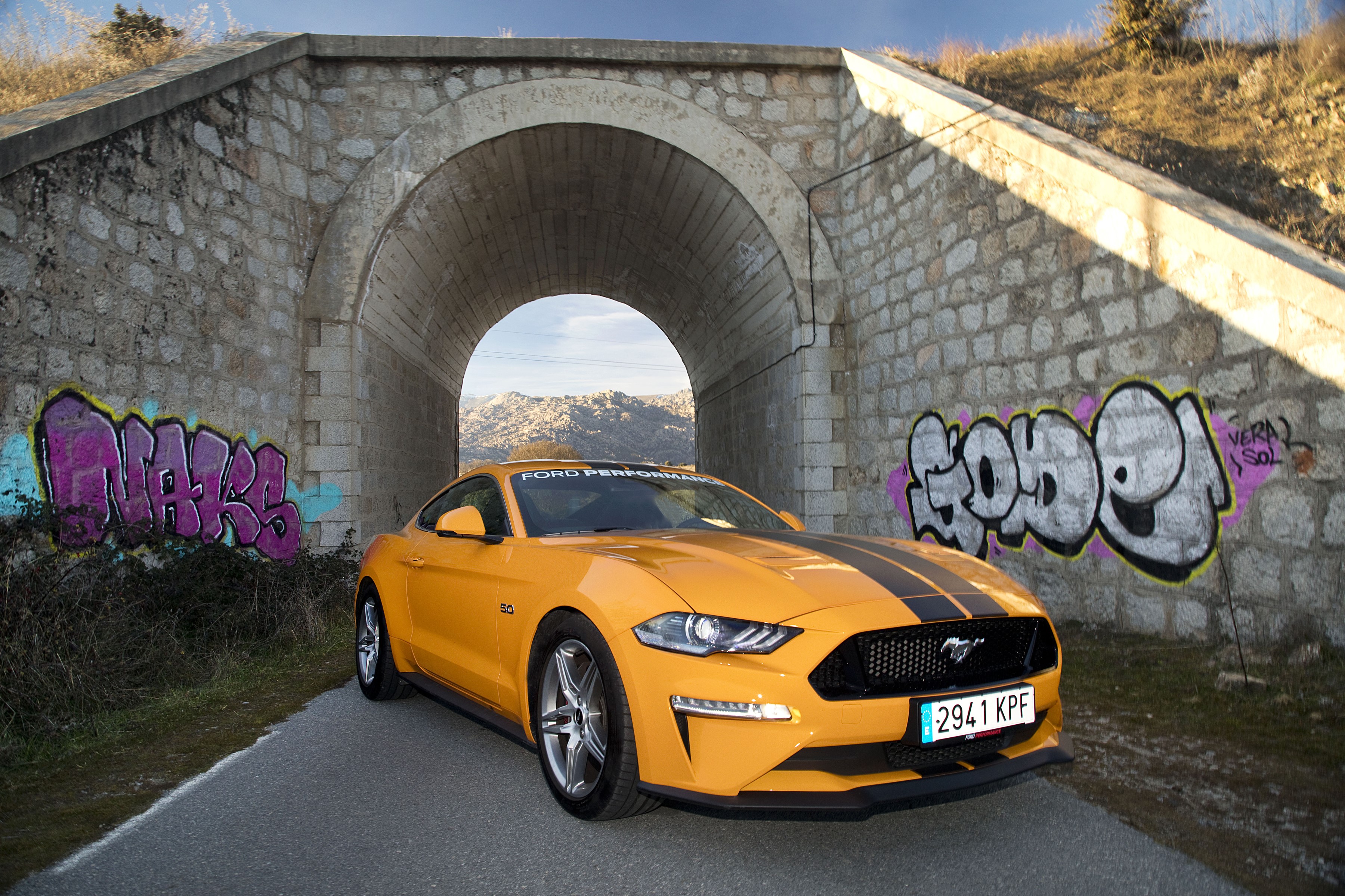 Yellow Ford Mustang GT with racing stripes under a bridge HD Wallpaper