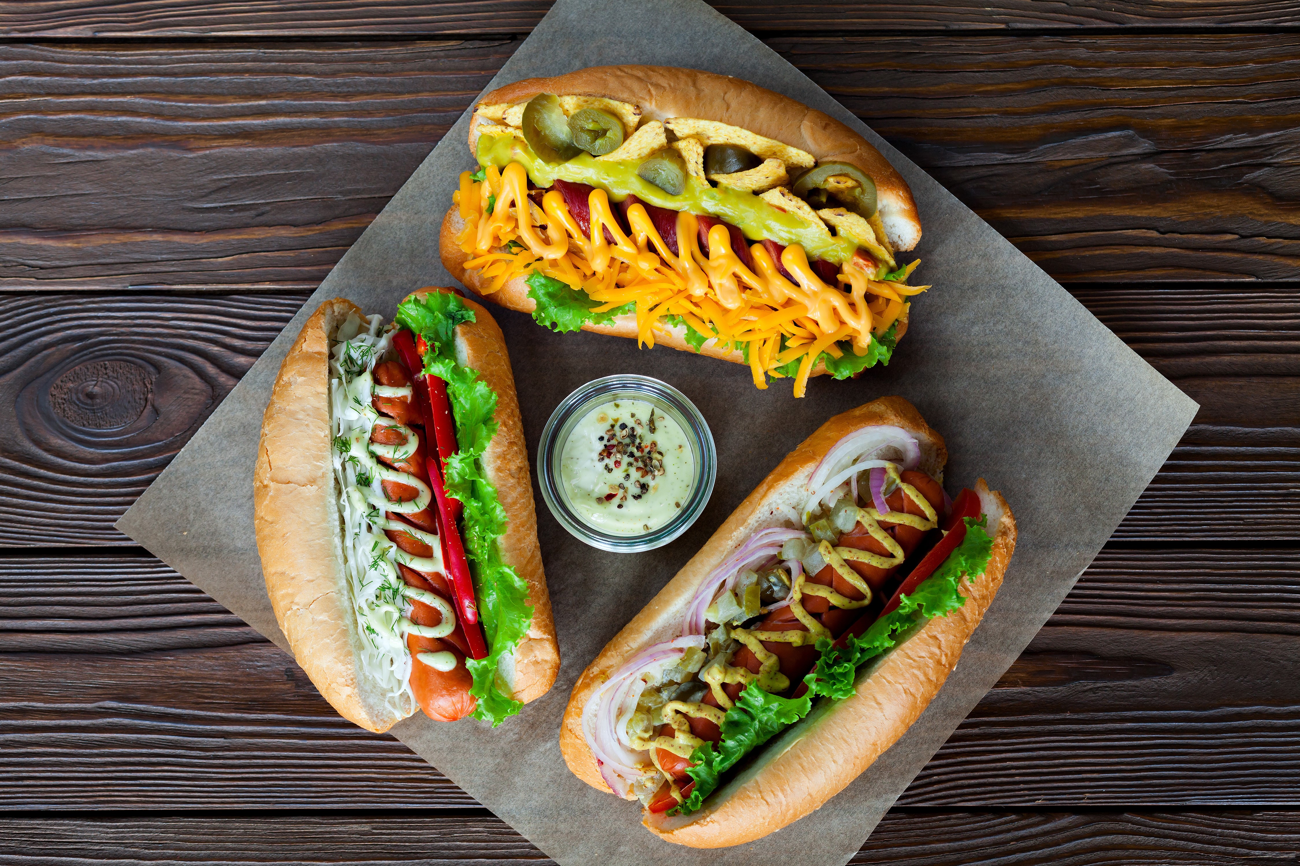 Three hot dogs with various toppings and a dipping sauce HD Wallpaper