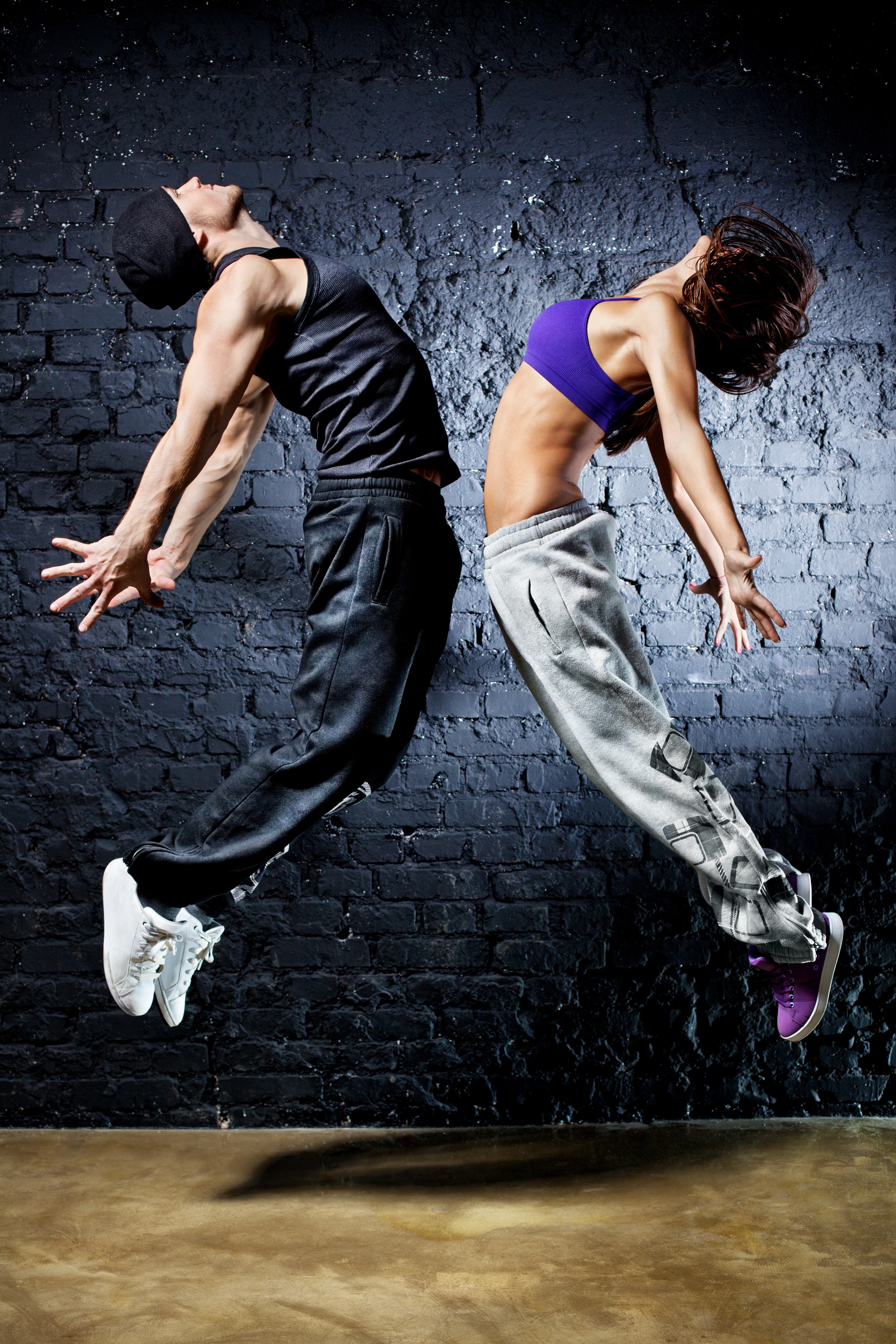 Two dancers jumping in front of a brick wall HD Phone Wallpaper
