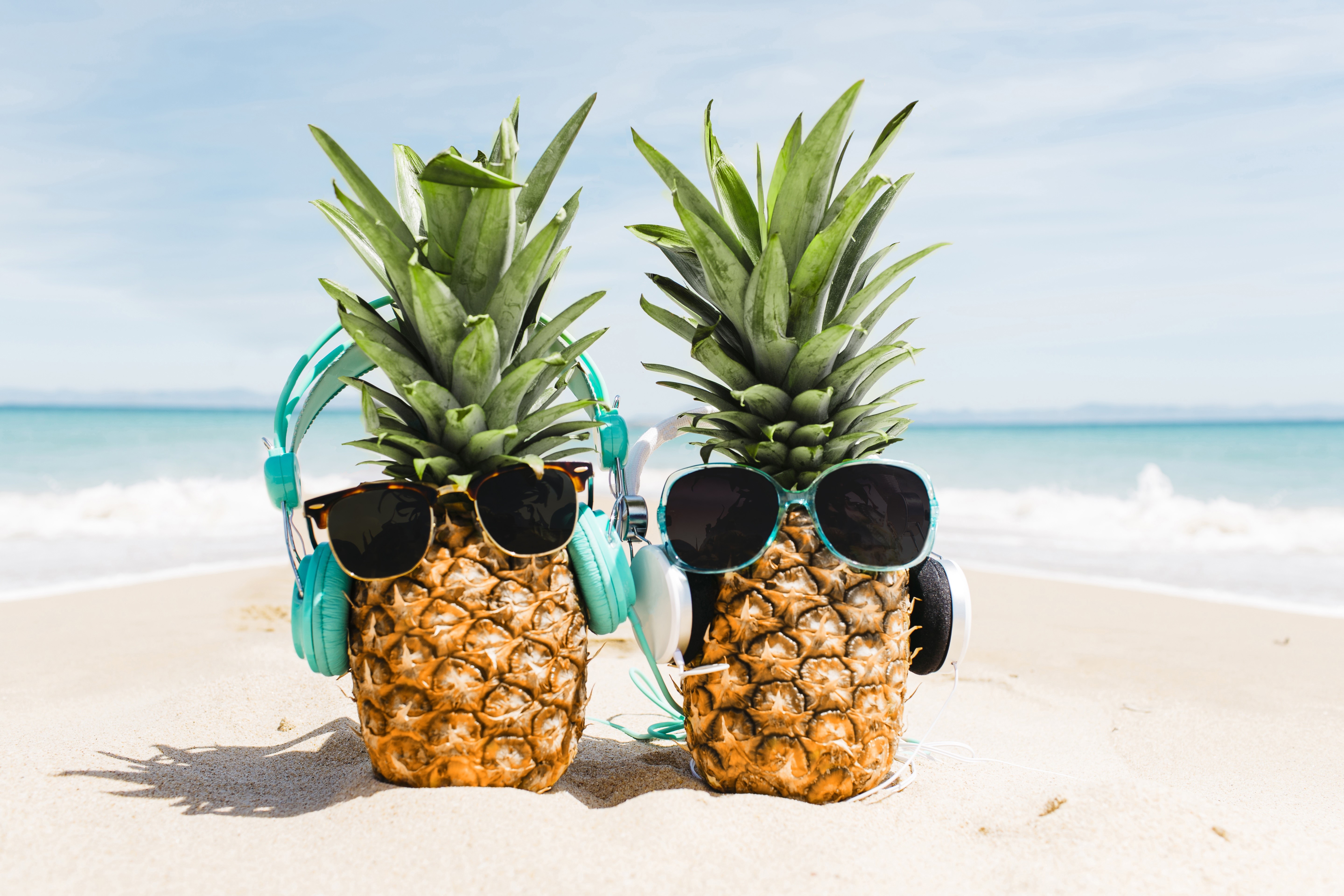 Two pineapples with sunglasses and headphones on a beach HD Wallpaper