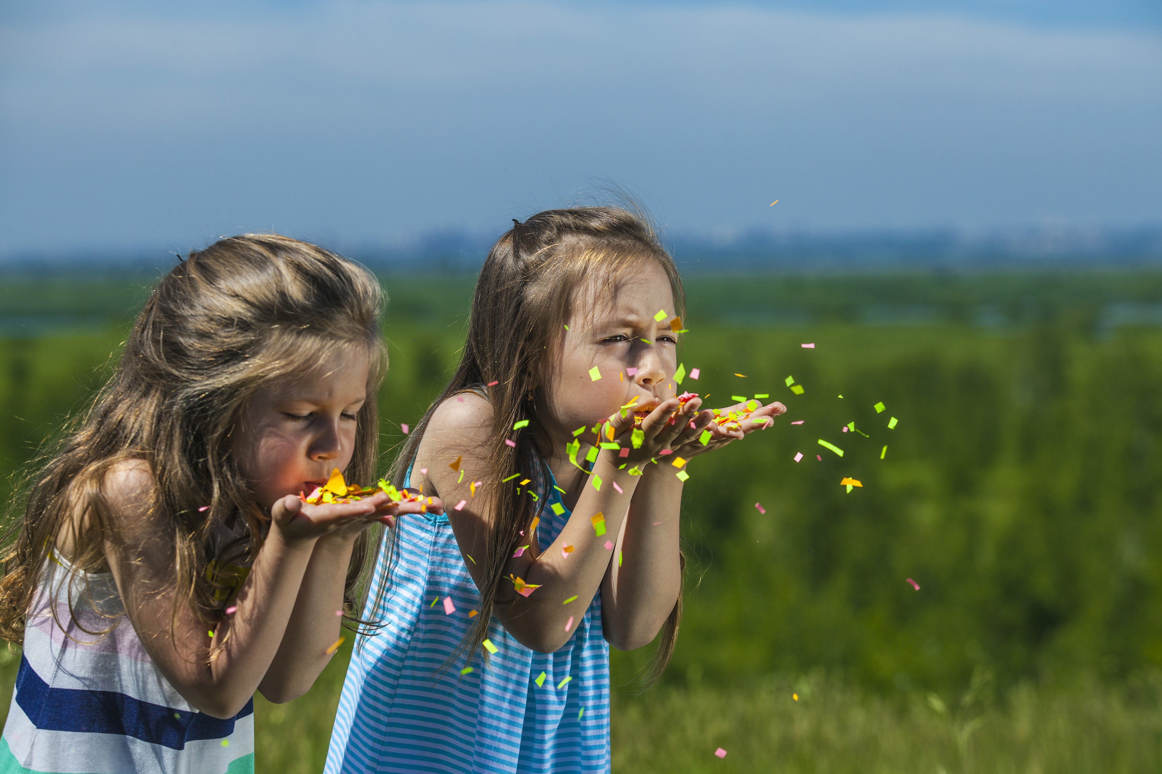 Two young girls blowing confetti outdoors HD Wallpaper