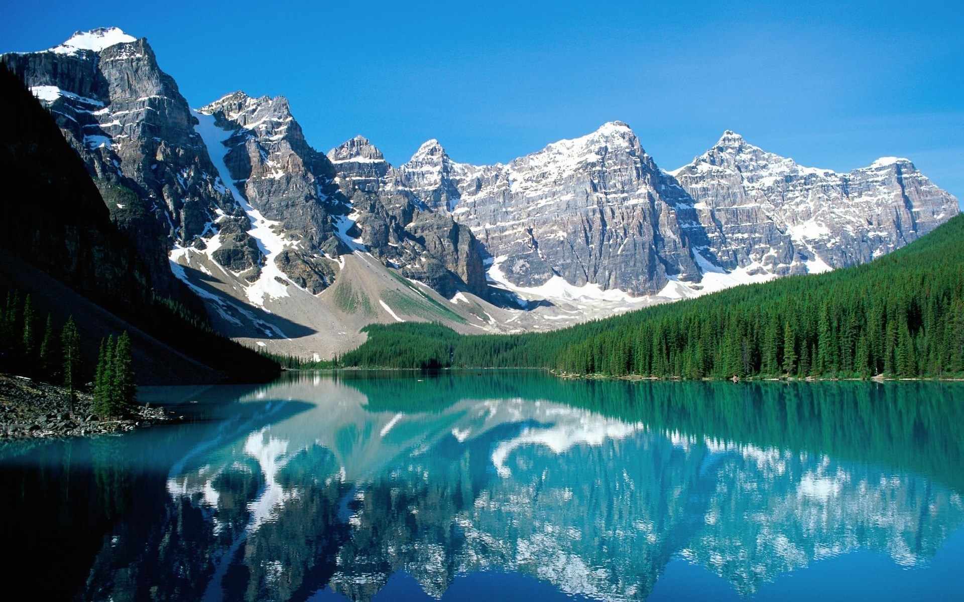 Snow-capped mountains reflected in a turquoise lake with pine trees HD Wallpaper