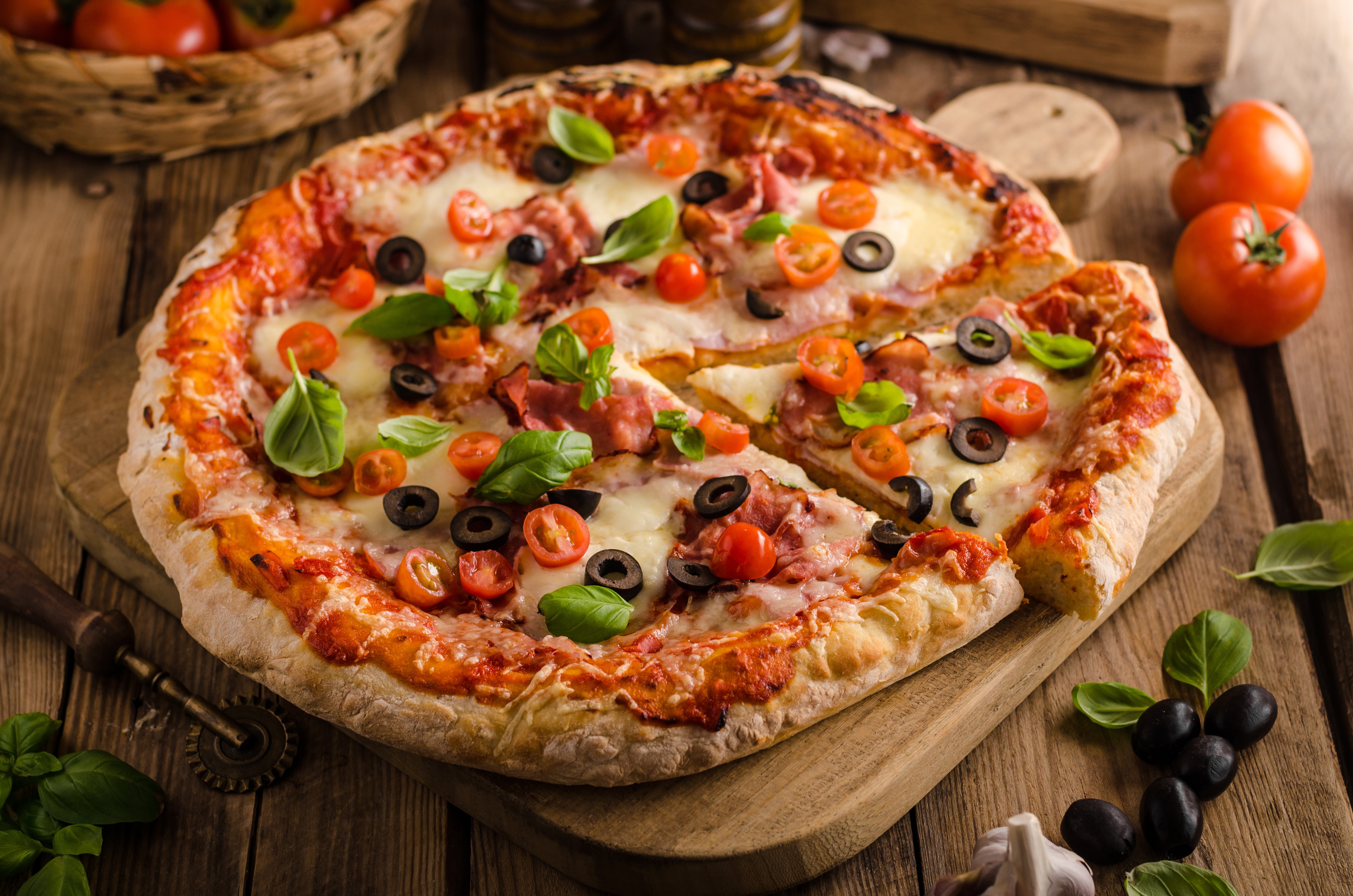 Pizza with tomatoes, olives, and basil on a cutting board HD Wallpaper