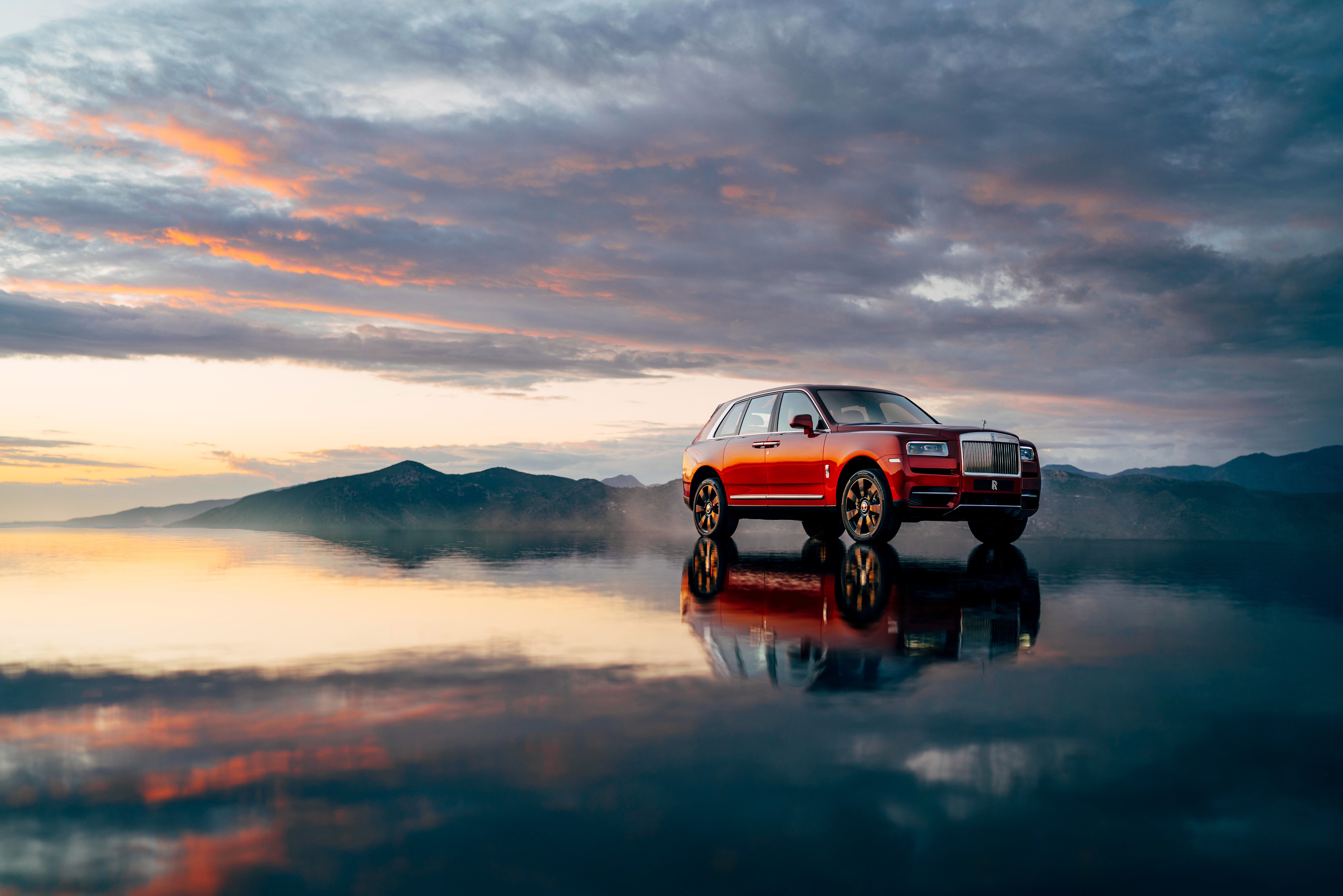 Red Rolls-Royce Cullinan on reflective surface at sunset HD Wallpaper