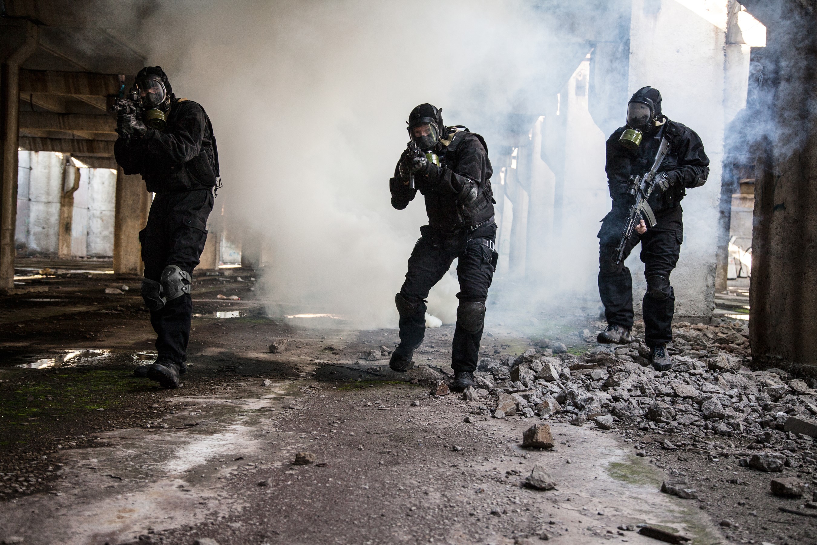 Three soldiers in gas masks with assault rifles in a ruined building HD Wallpaper