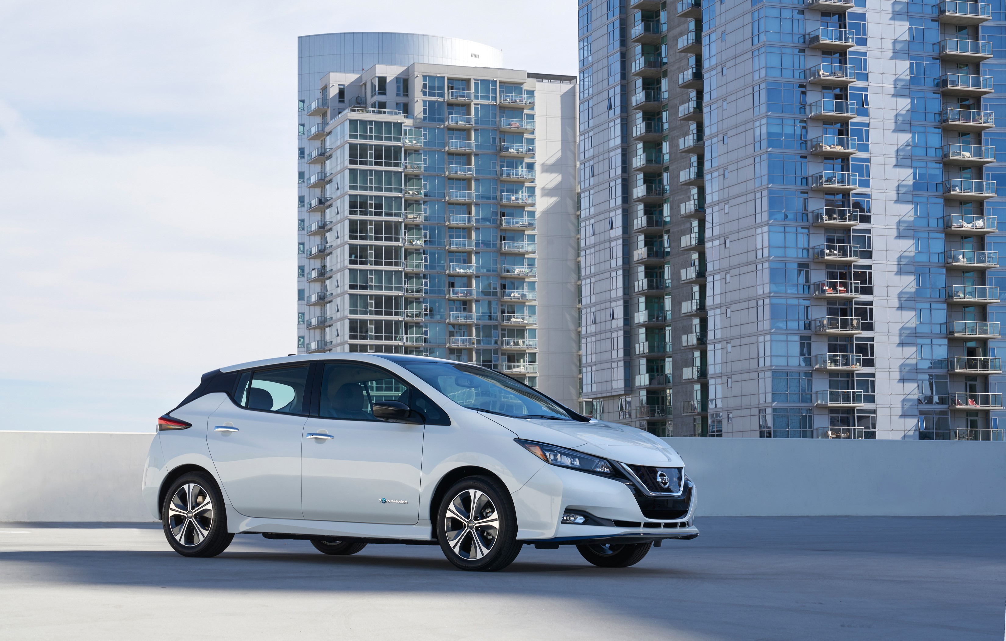 White 2019 Nissan Leaf e parked in front of modern buildings HD Wallpaper