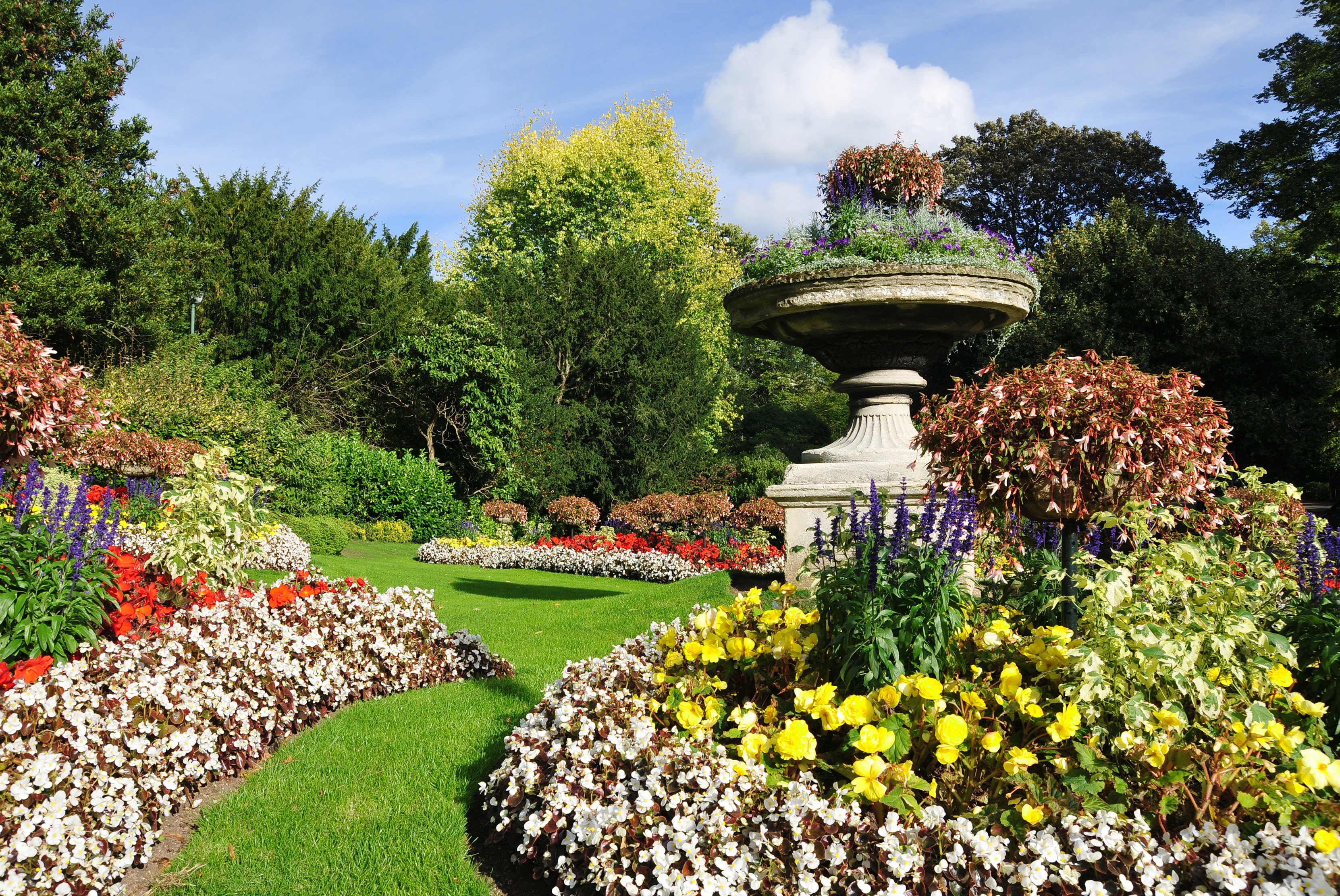Beautifully manicured park garden with colorful flower beds and a stone urn HD Wallpaper
