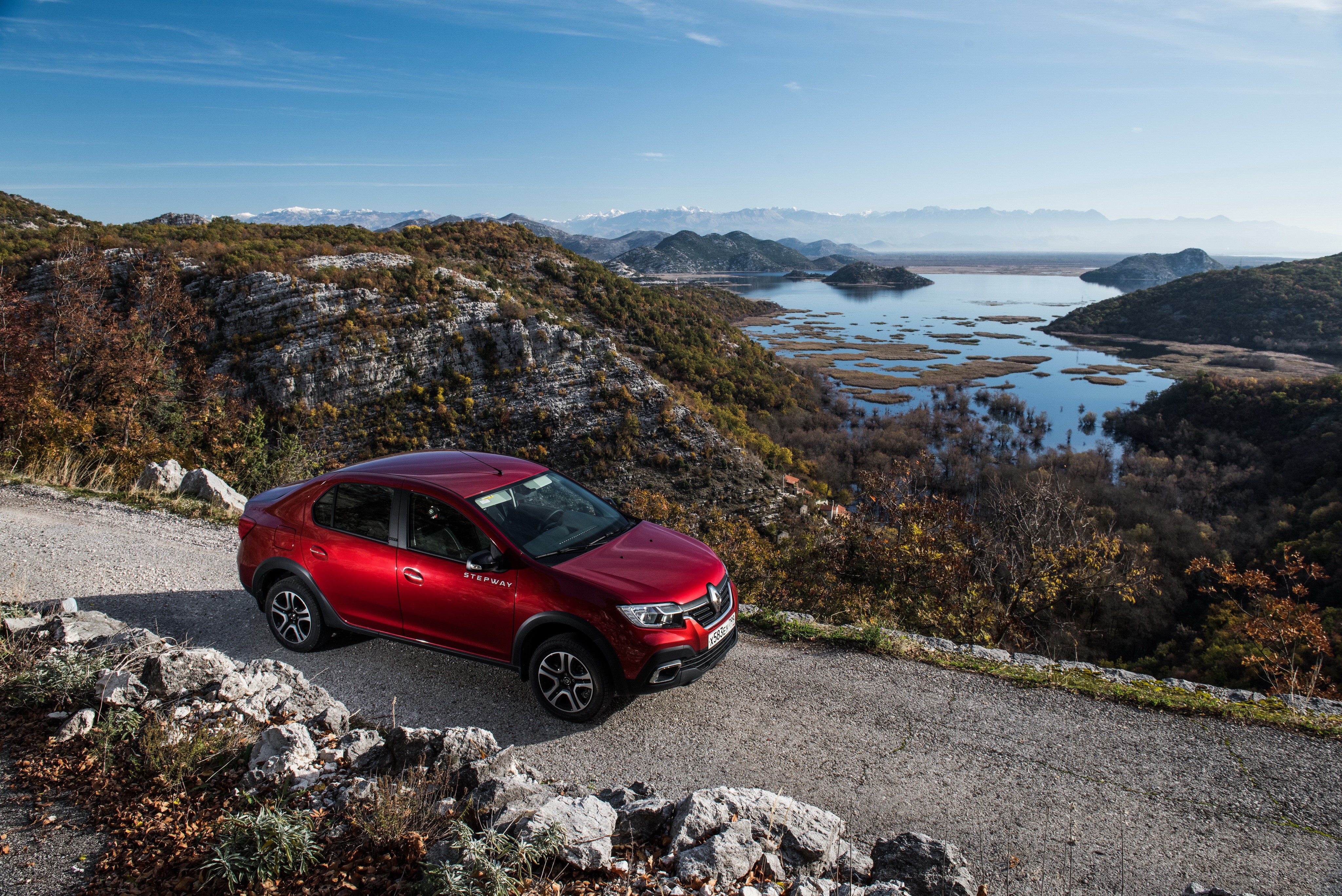 Red Renault Logan Stepway on a mountain road overlooking a lake HD Wallpaper