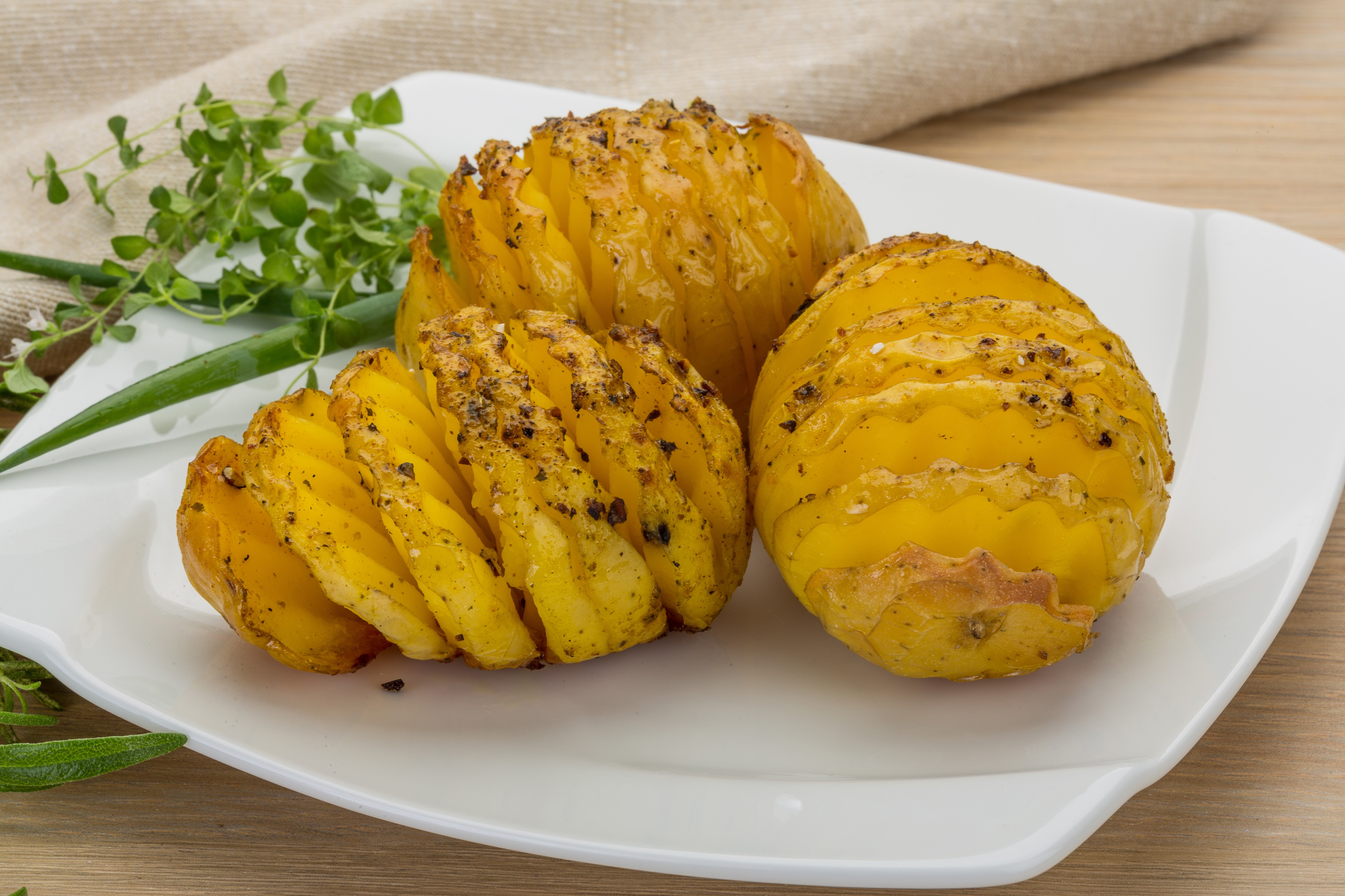 Hasselback Potatoes on a White Plate with Herbs HD Wallpaper