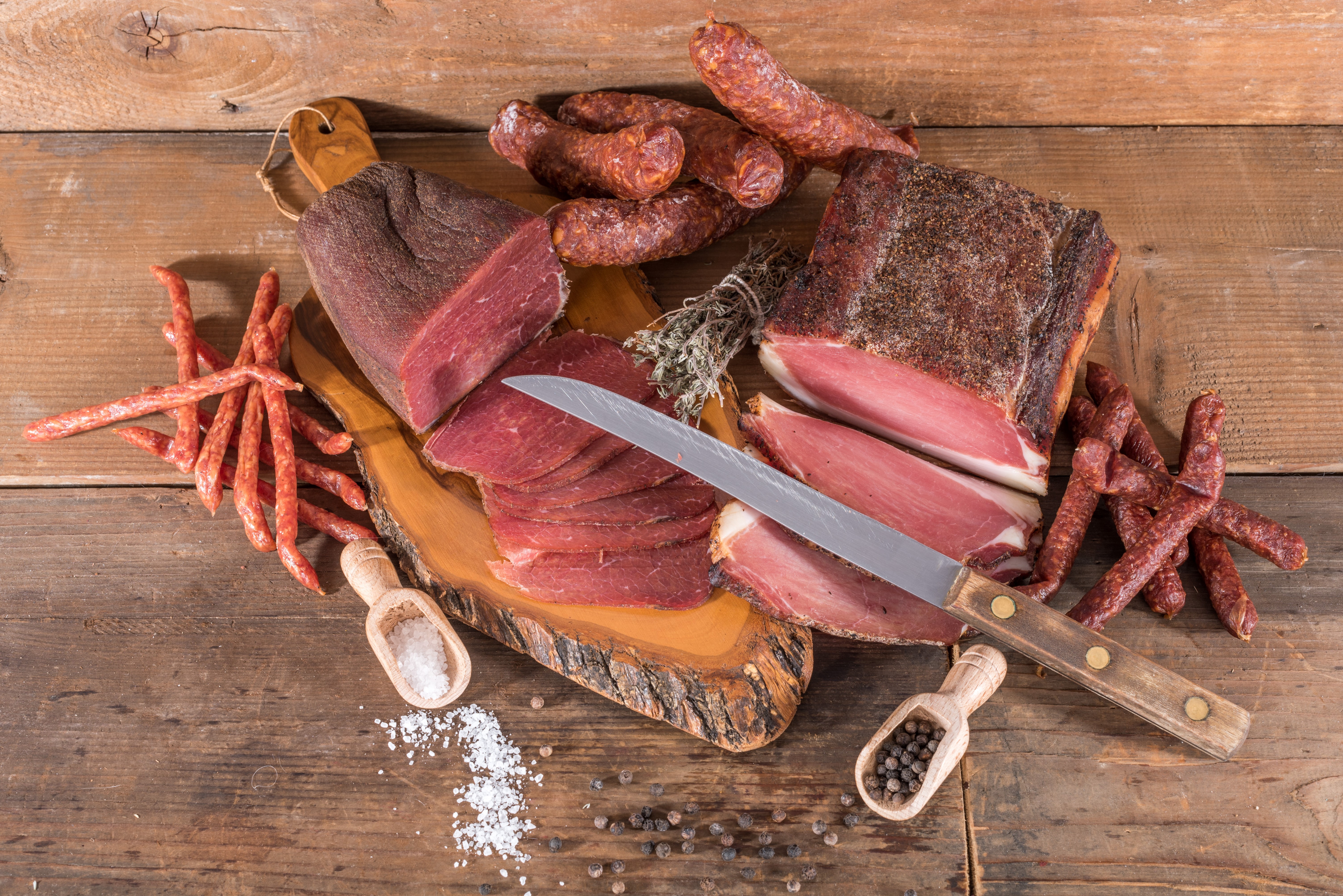 Assortment of cured meats and sausages on a wooden board HD Wallpaper