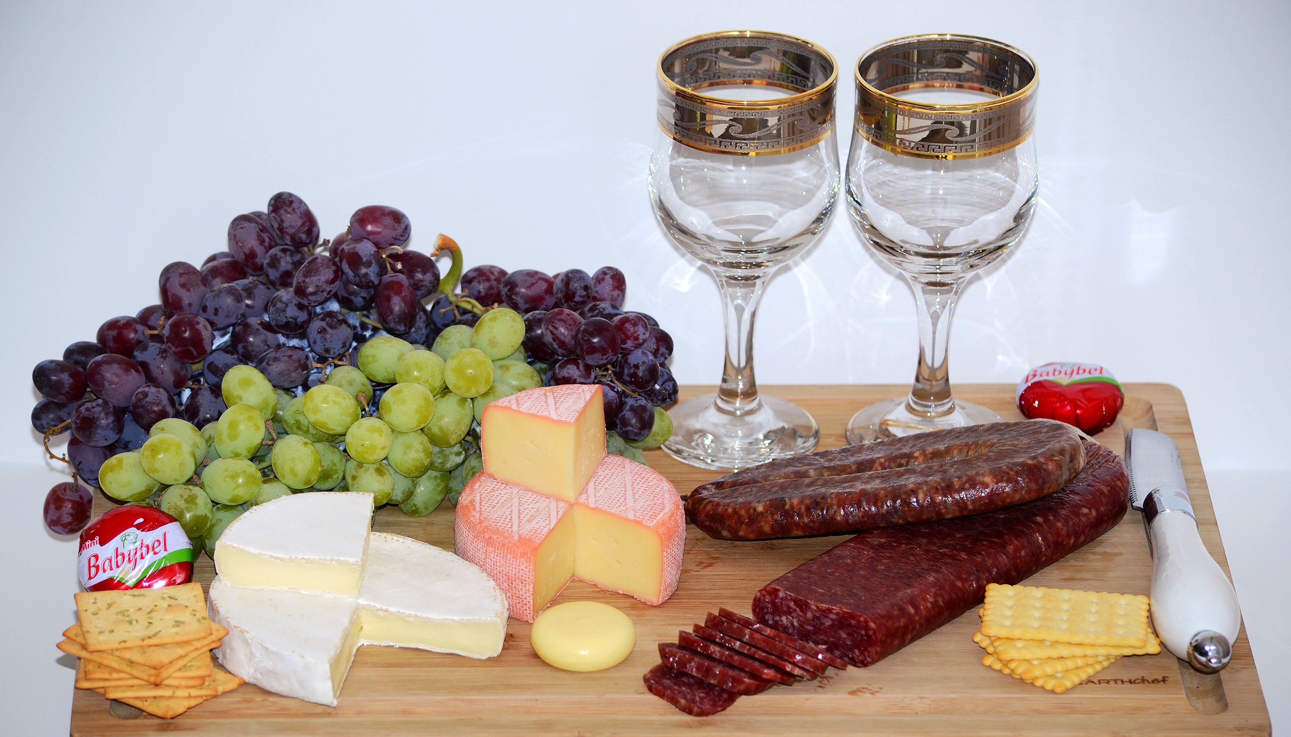 Cheese, Grapes, Sausage, Crackers, and Stemware on a Cutting Board HD Wallpaper