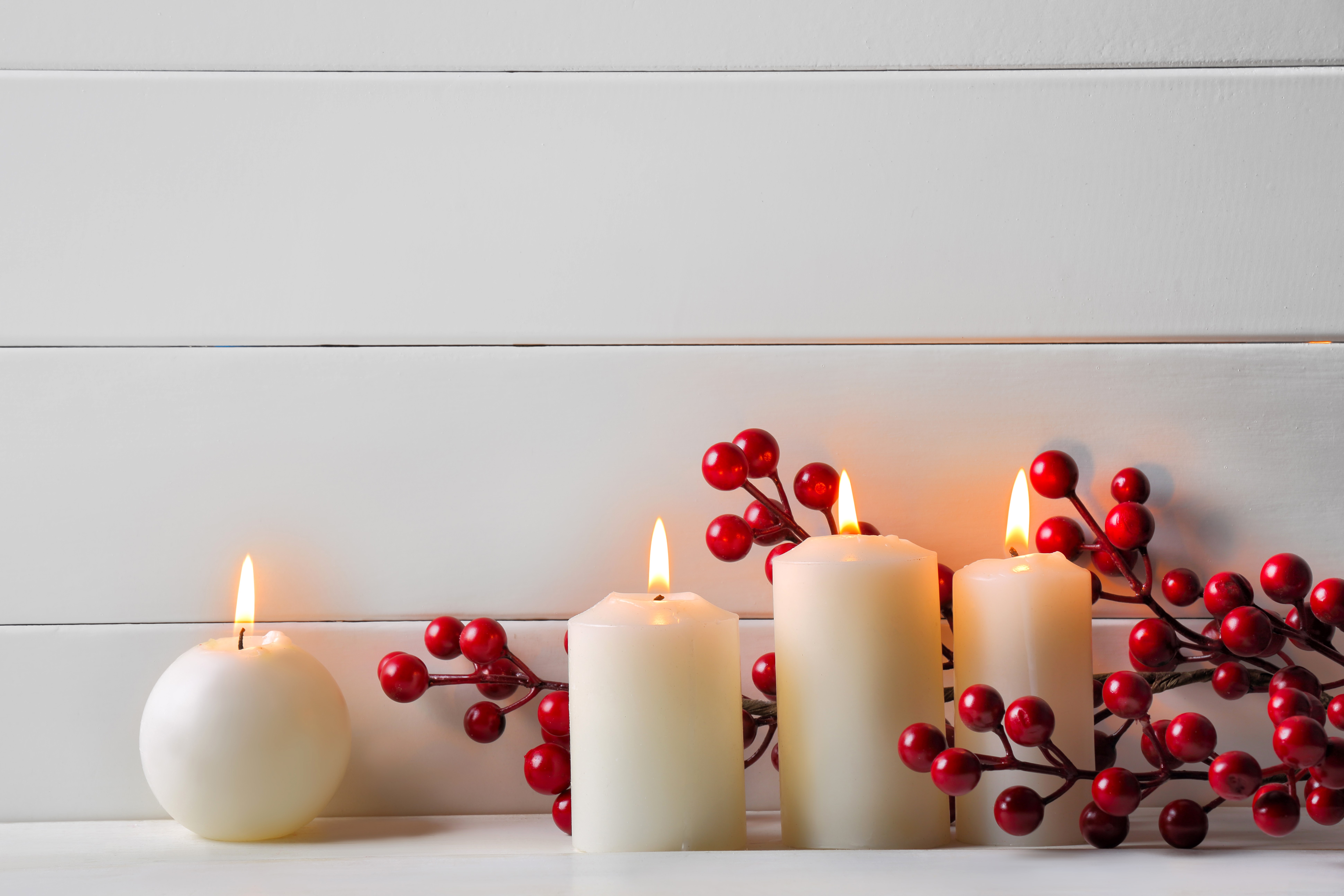Four lit candles with red berries on white wooden background HD Wallpaper
