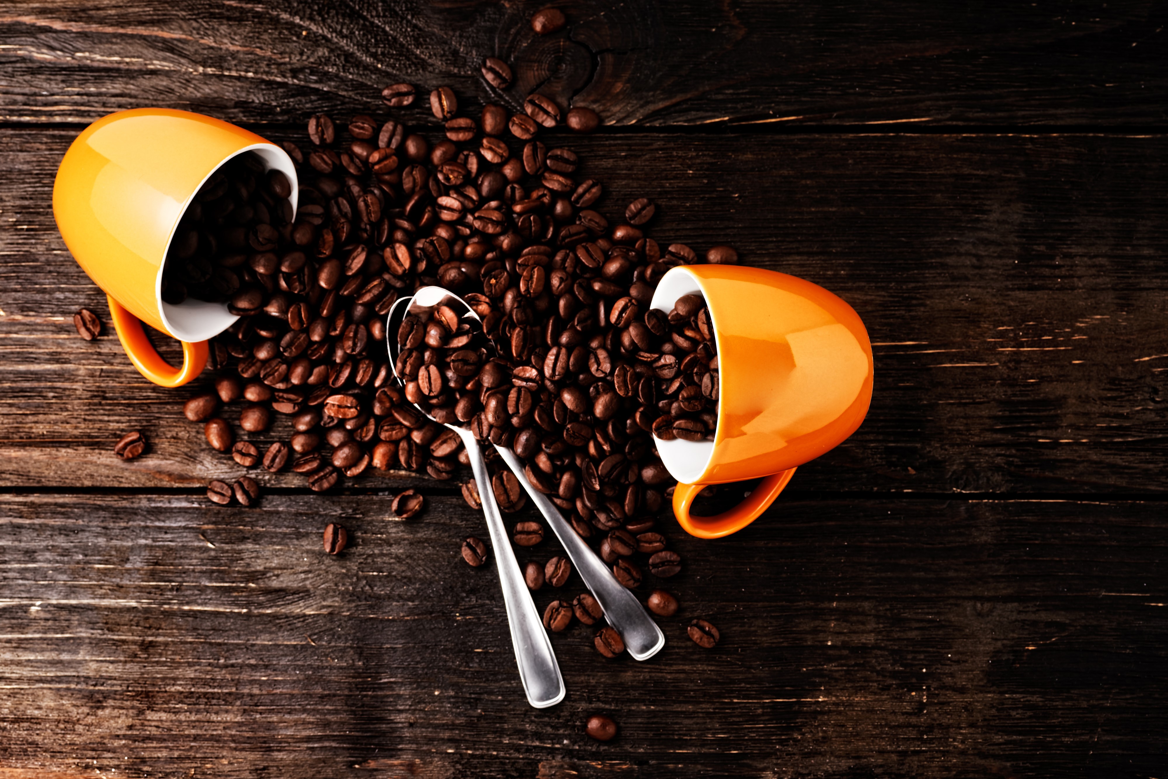 Two orange cups spilling coffee beans with spoons on wood HD Wallpaper
