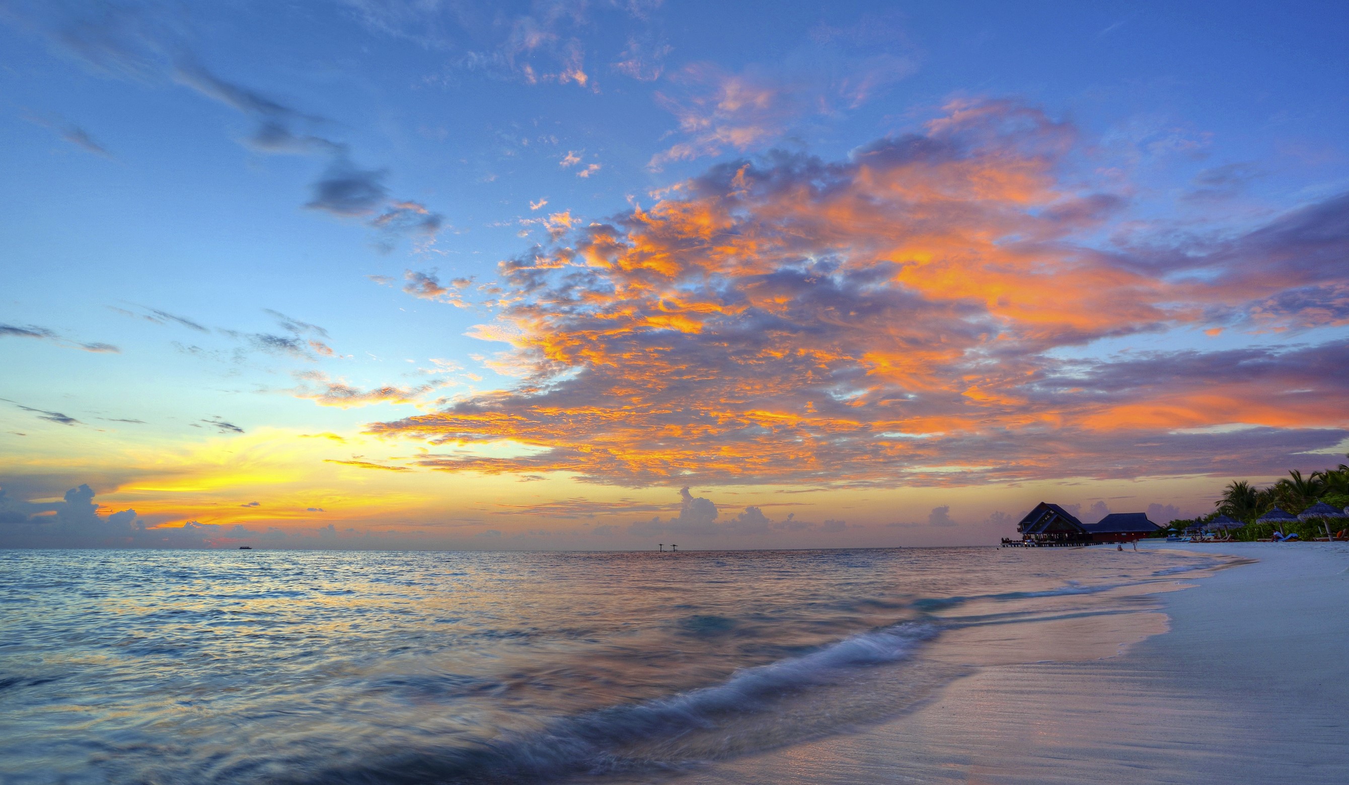 Sunset over the ocean with clouds and beach huts HD Wallpaper