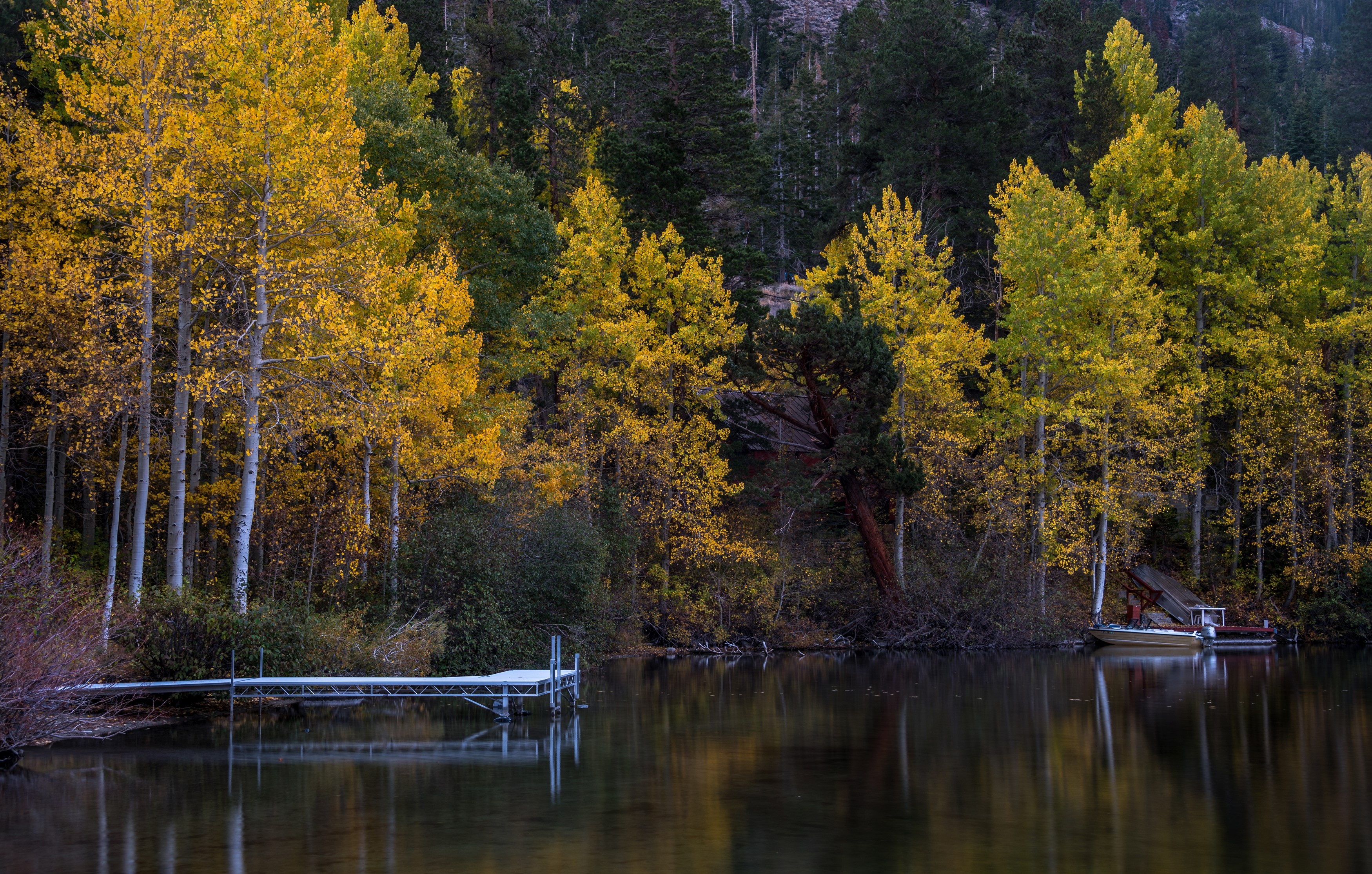 Autumn trees reflected in a lake with a dock and boats HD Wallpaper