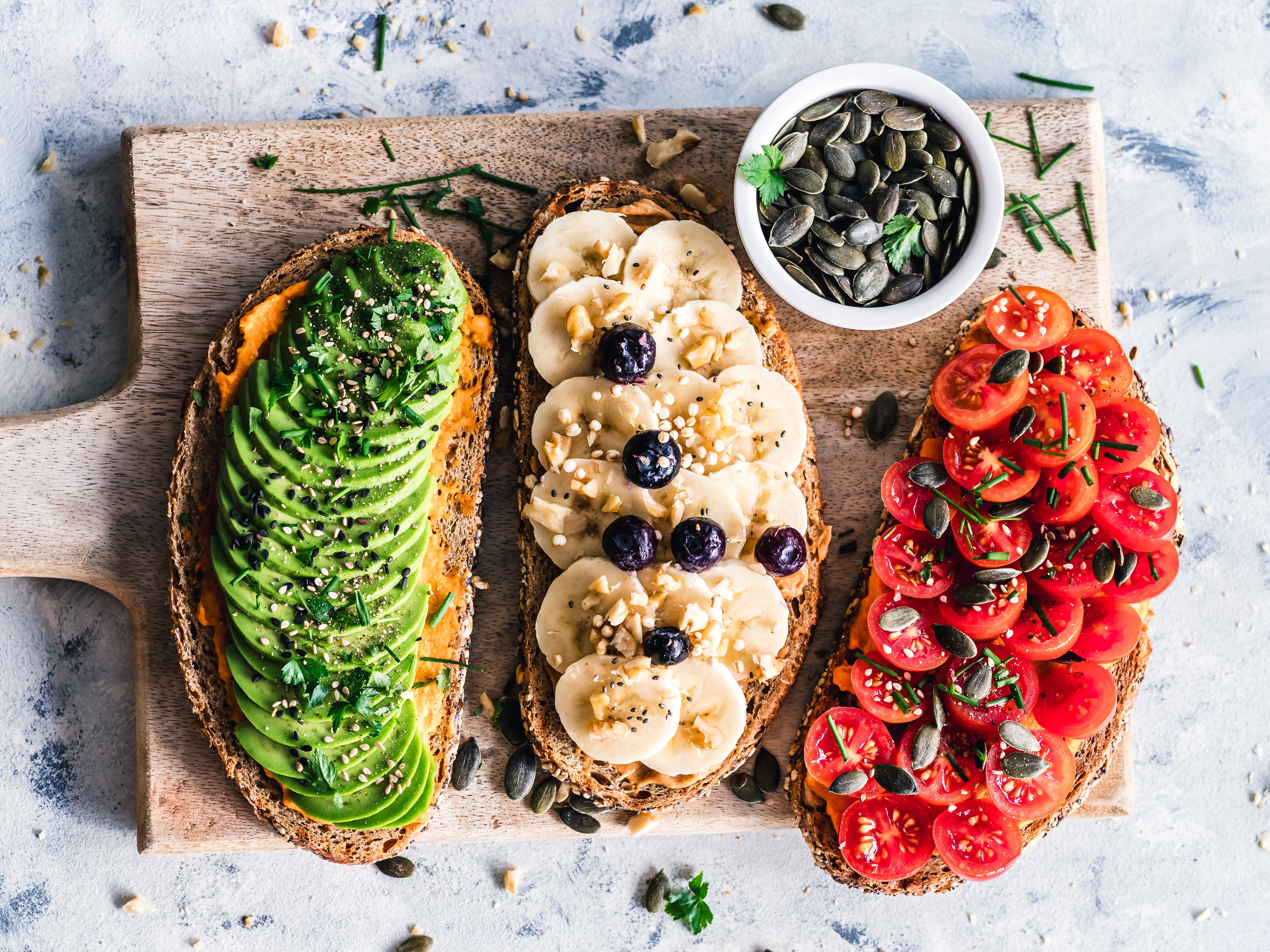 Three toasts with avocado, banana, and tomatoes on a cutting board HD Wallpaper