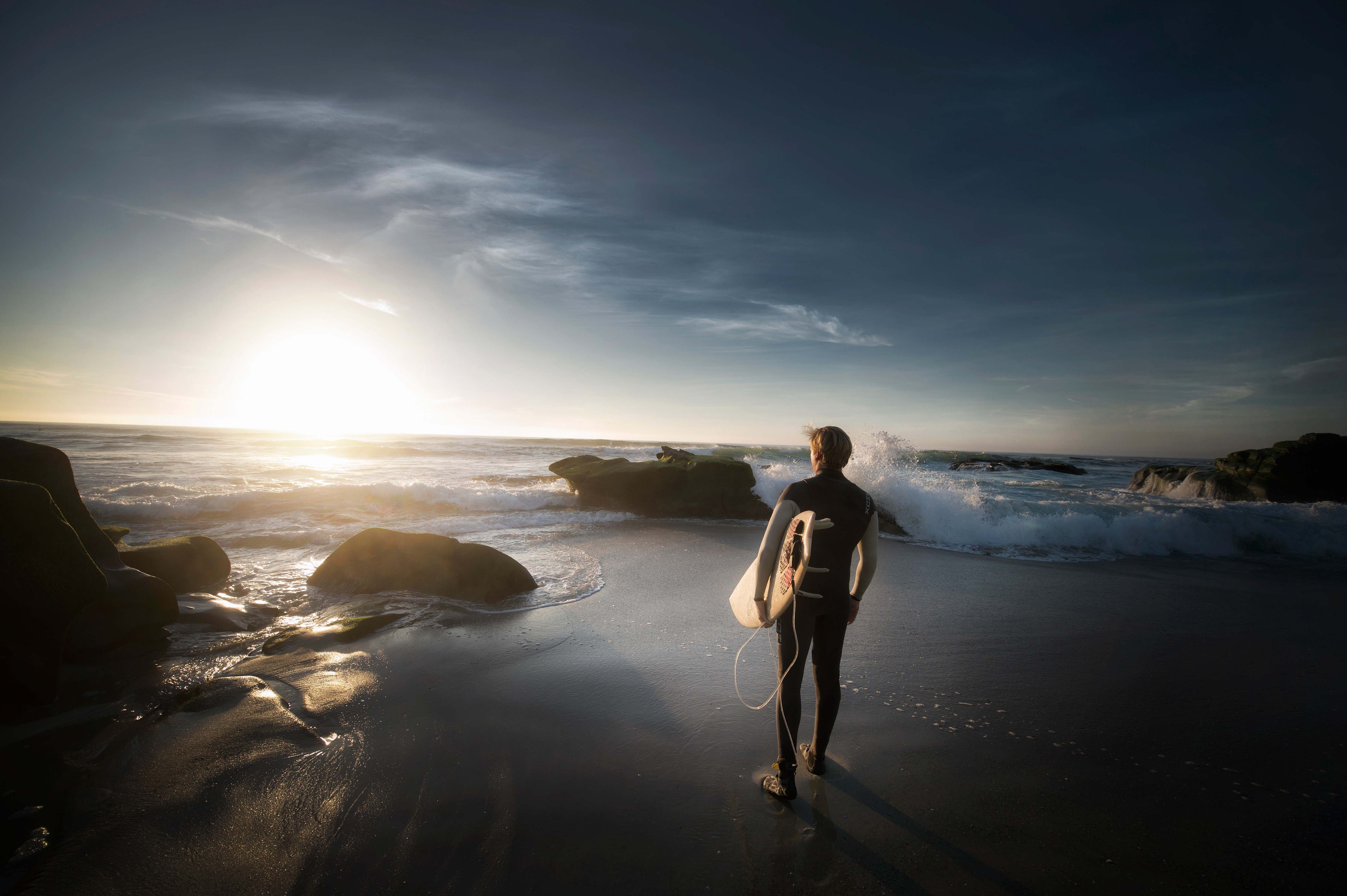 Surfer with surfboard on beach at sunset HD Wallpaper