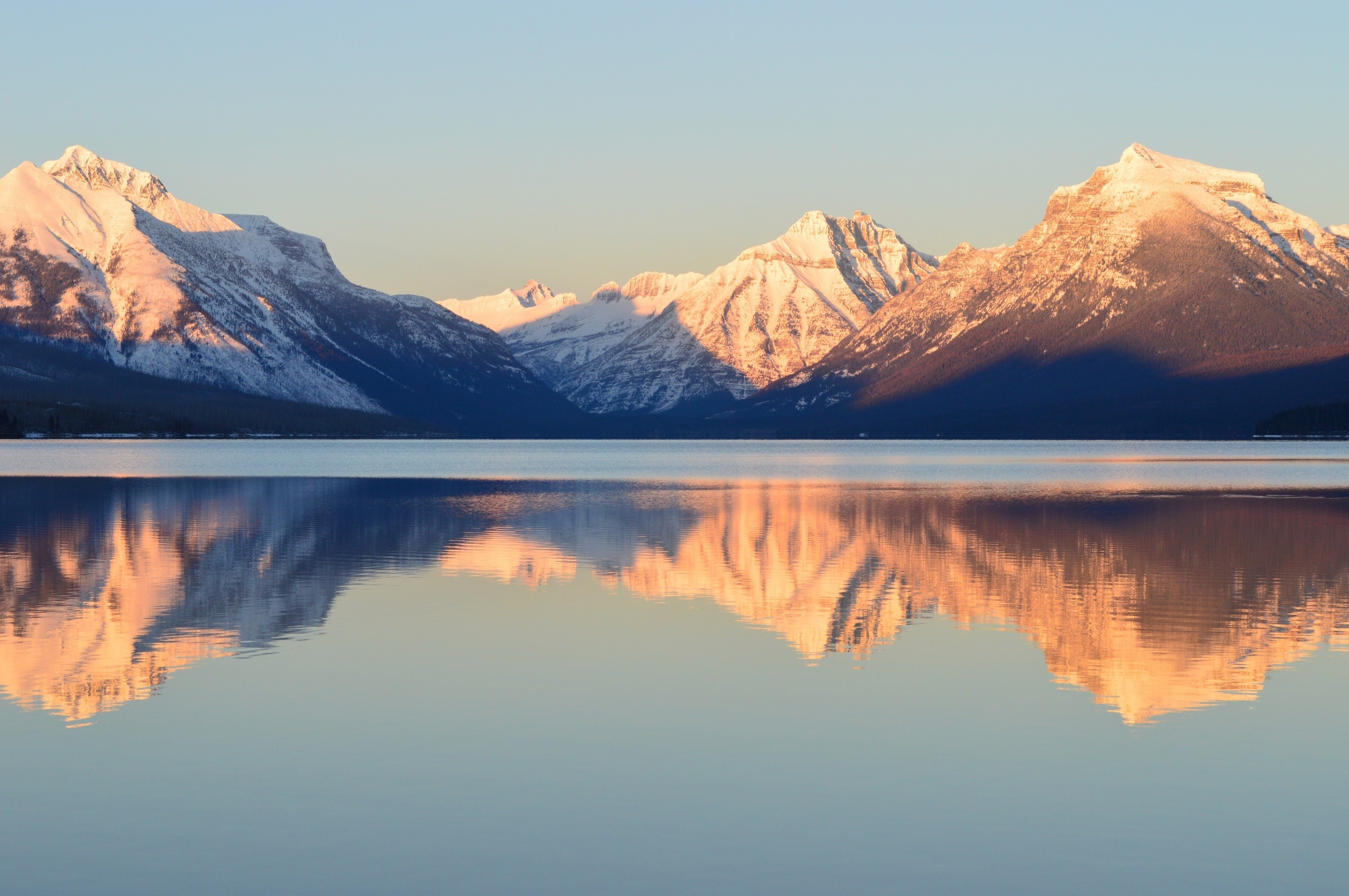Snow-capped mountains reflected in a calm lake at sunrise HD Wallpaper