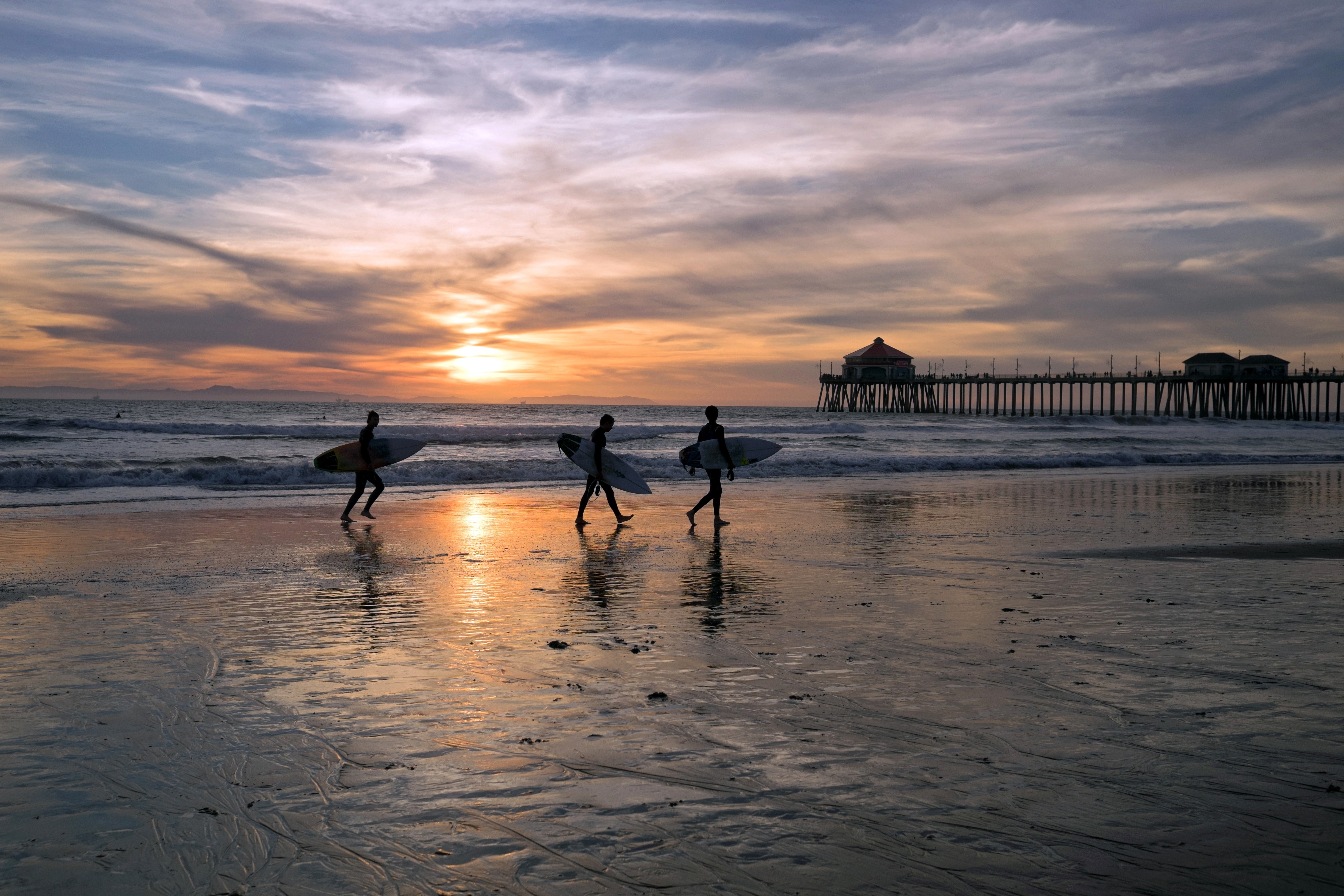 Surfers walking on beach at sunset with pier HD Wallpaper