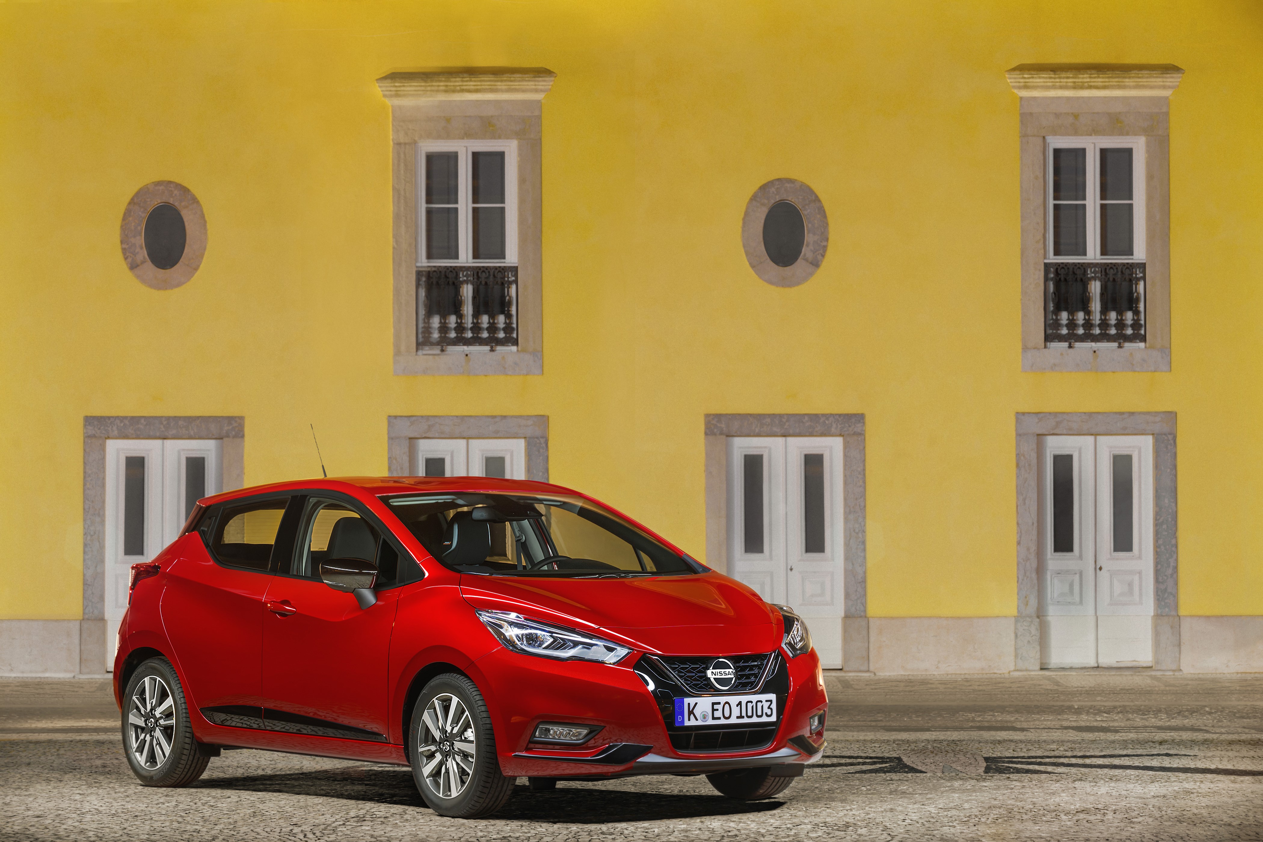 Red Nissan Micra in front of yellow building HD Wallpaper