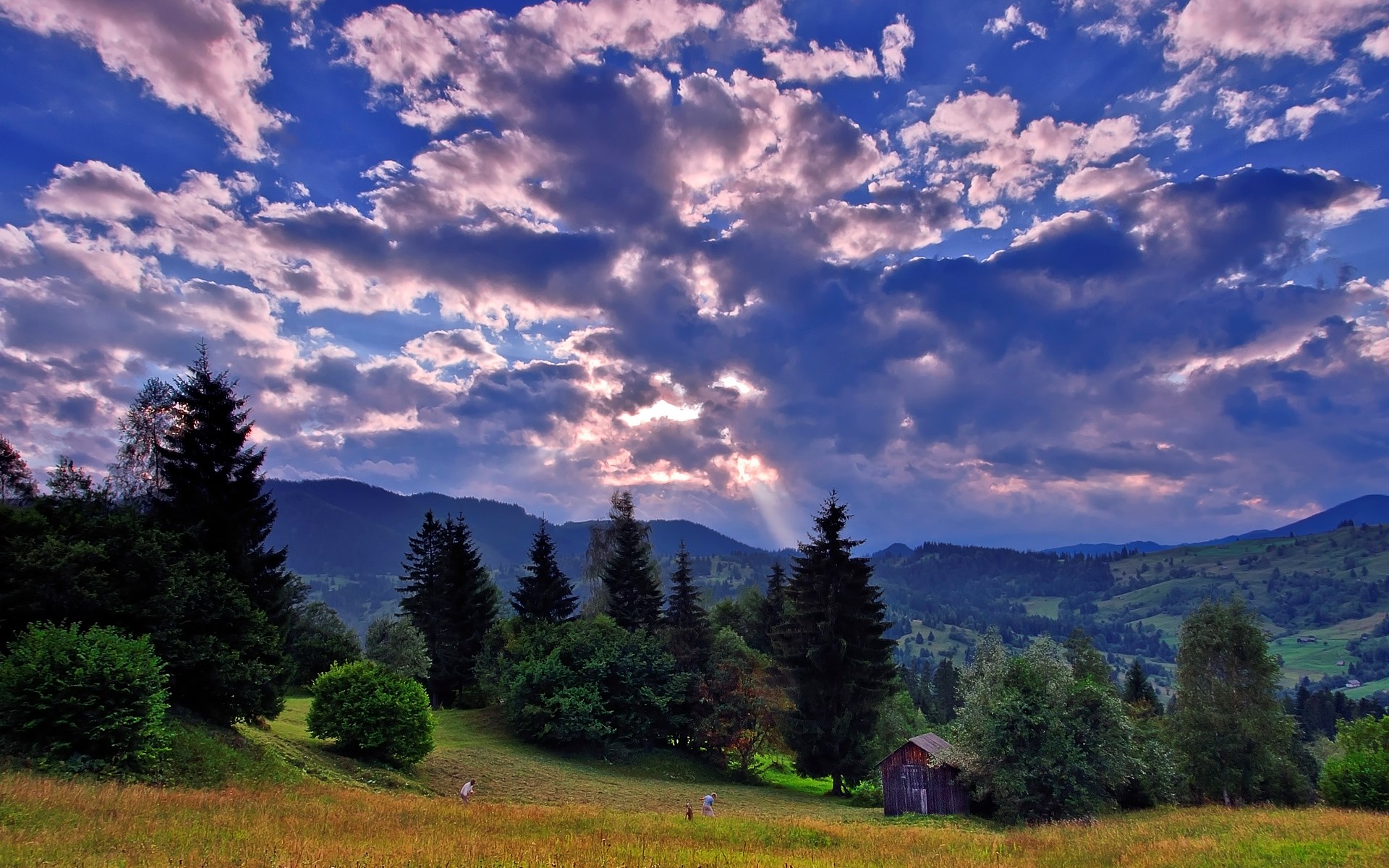 Sunbeams through clouds over a mountain landscape with trees HD Wallpaper