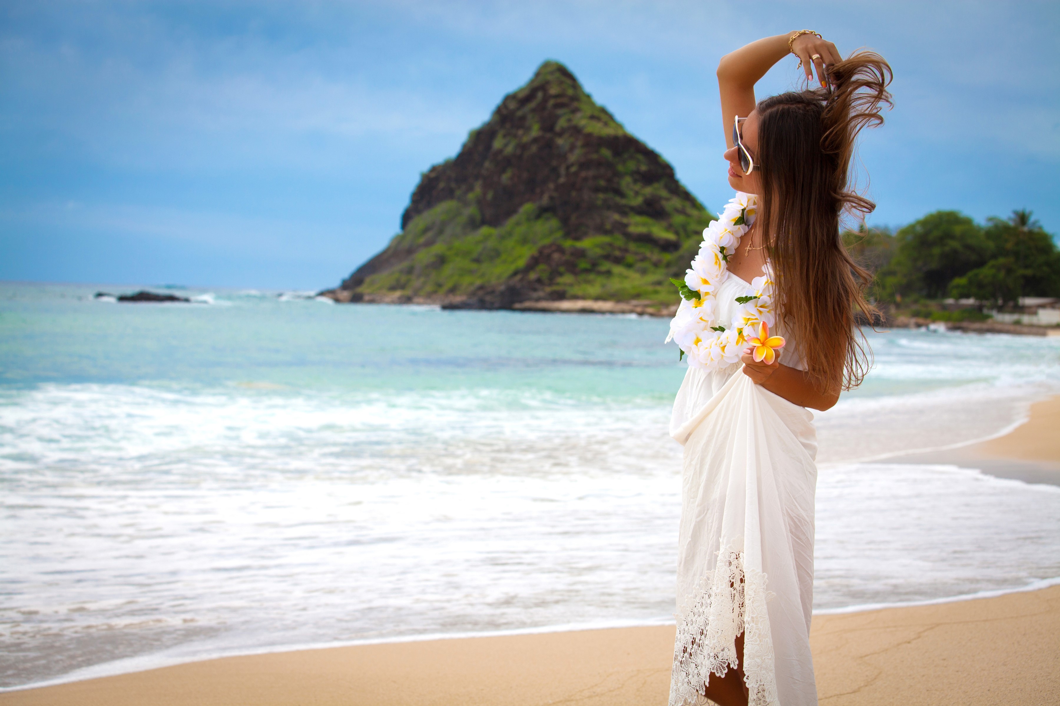 Woman in white dress with lei on beach with mountain background HD Wallpaper