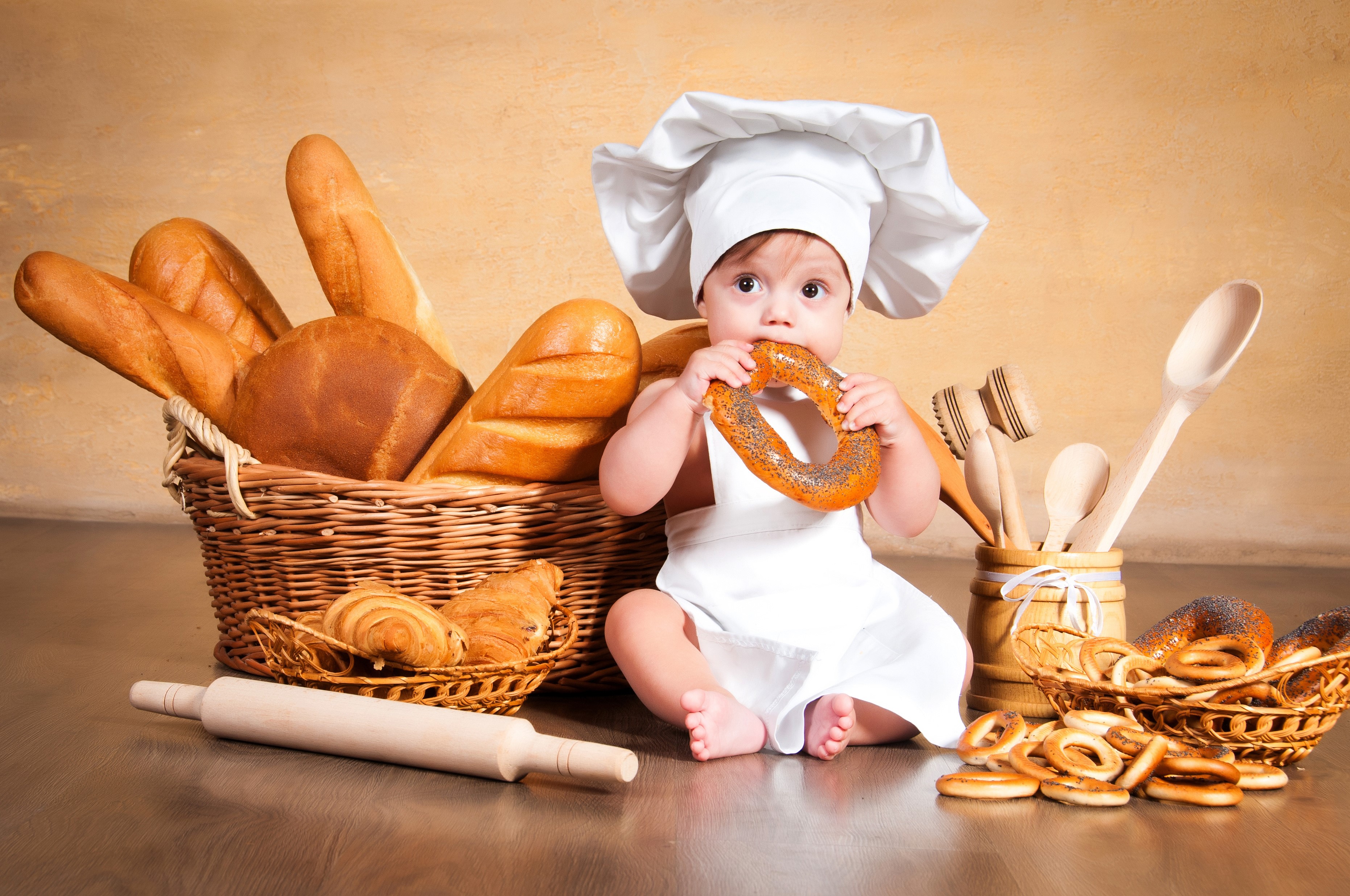 Baby chef eating a bagel with bread and pastries HD Wallpaper