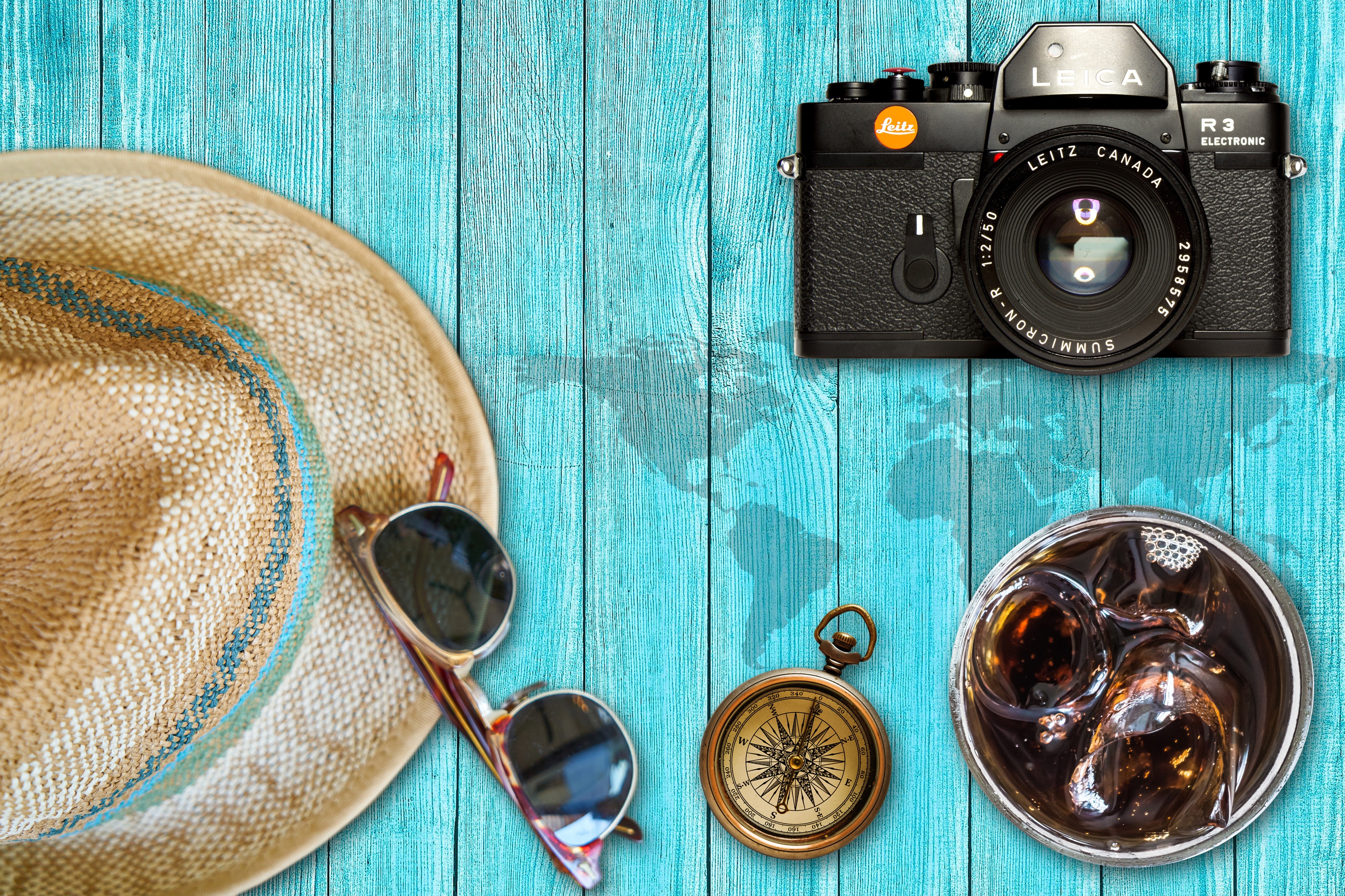 Travel essentials: Hat, sunglasses, camera, compass, and drink on wood HD Wallpaper
