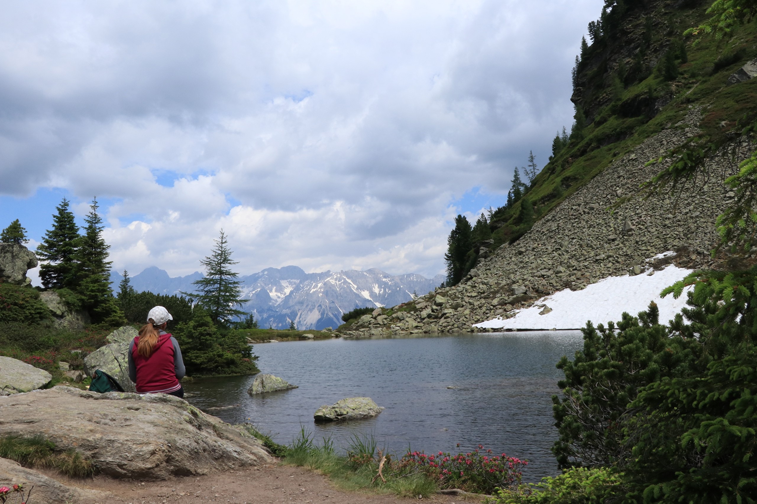 Girl sitting by a mountain lake with snow-capped peaks HD Wallpaper