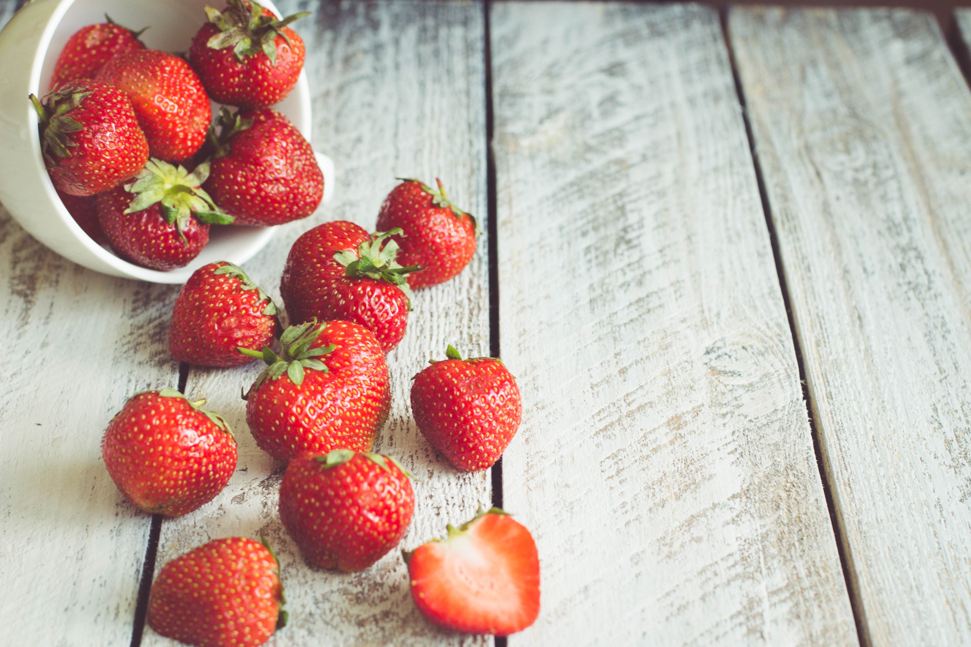 Strawberries spilling from a bowl onto wooden planks HD Wallpaper