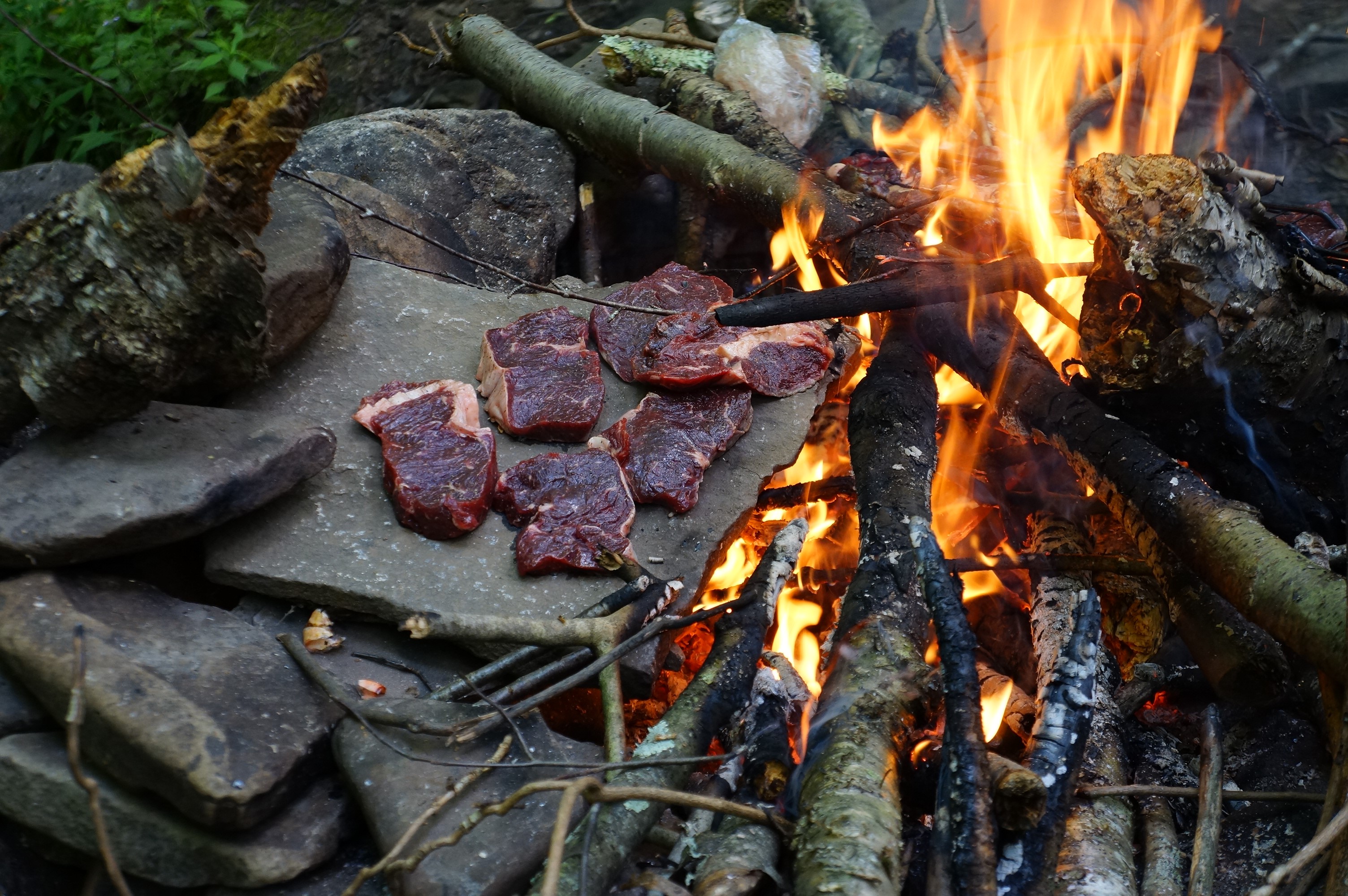 Raw steaks cooking on stones by a bonfire HD Wallpaper