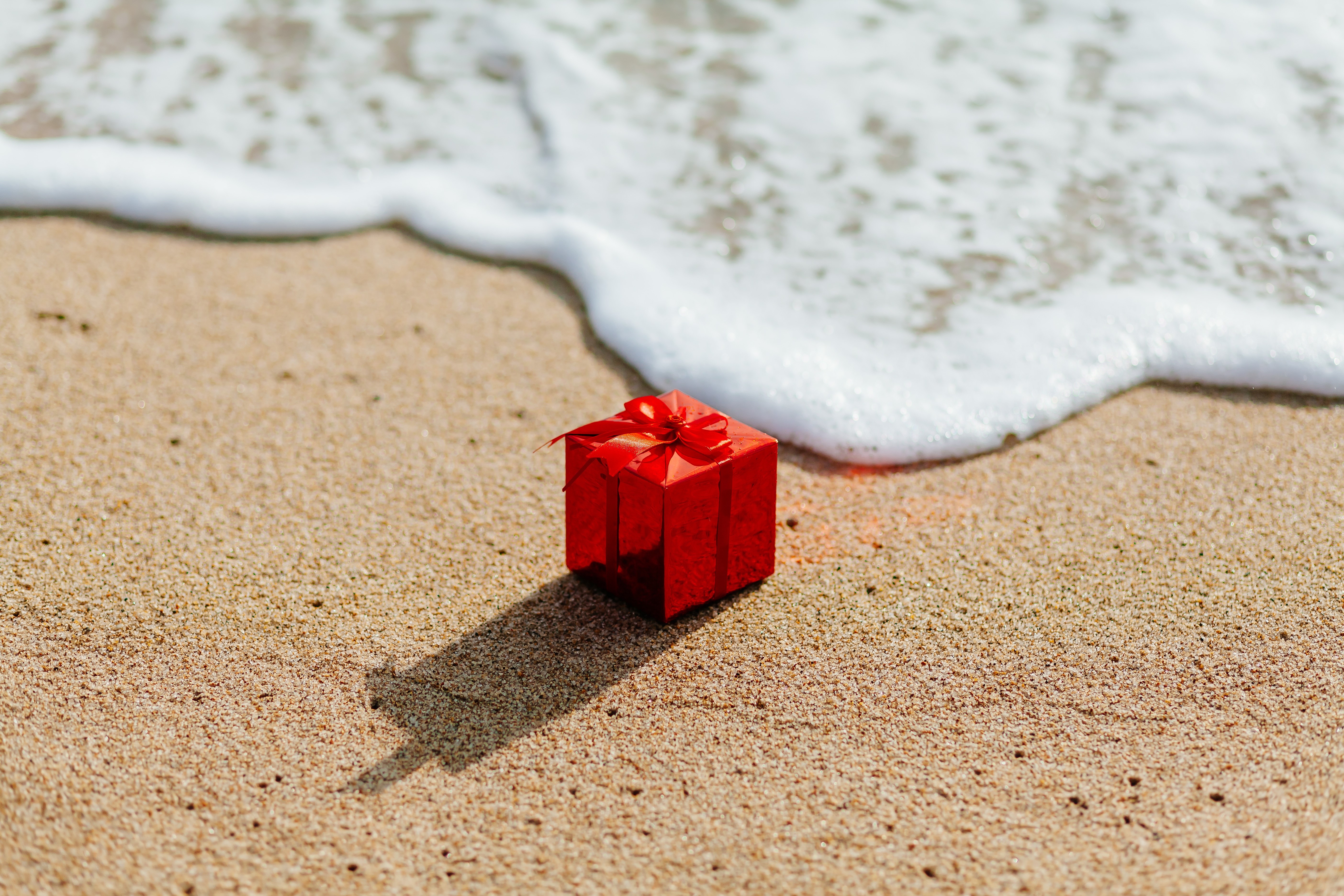 Red gift box on sand with waves HD Wallpaper