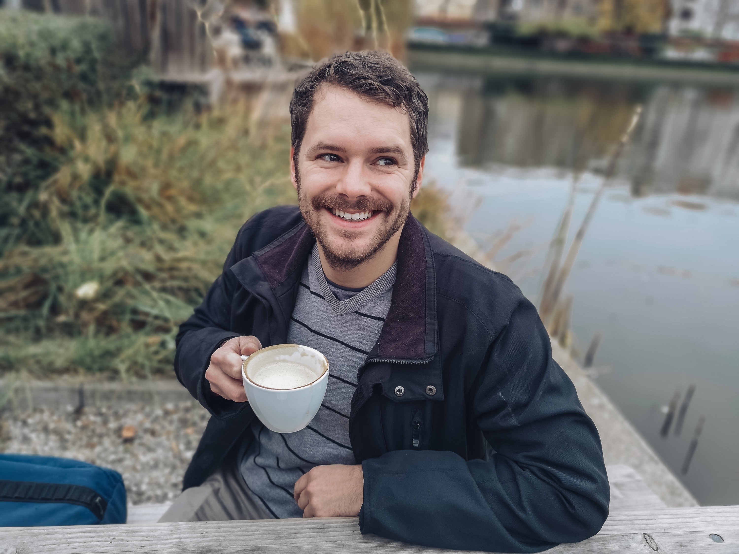 Man holding a cup of coffee by a lake HD Wallpaper