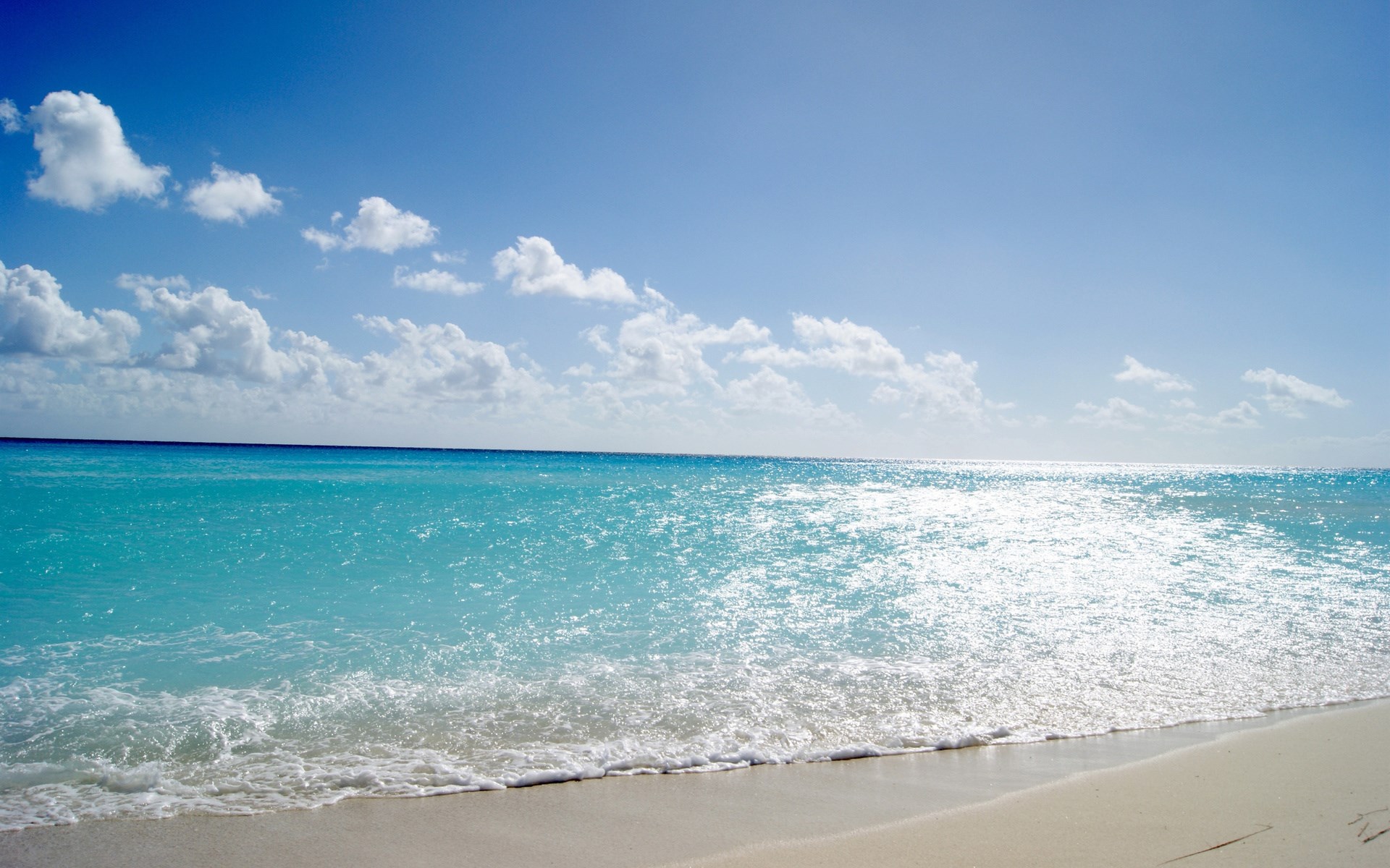 Turquoise ocean waves on a sandy beach under a blue sky with clouds HD Wallpaper