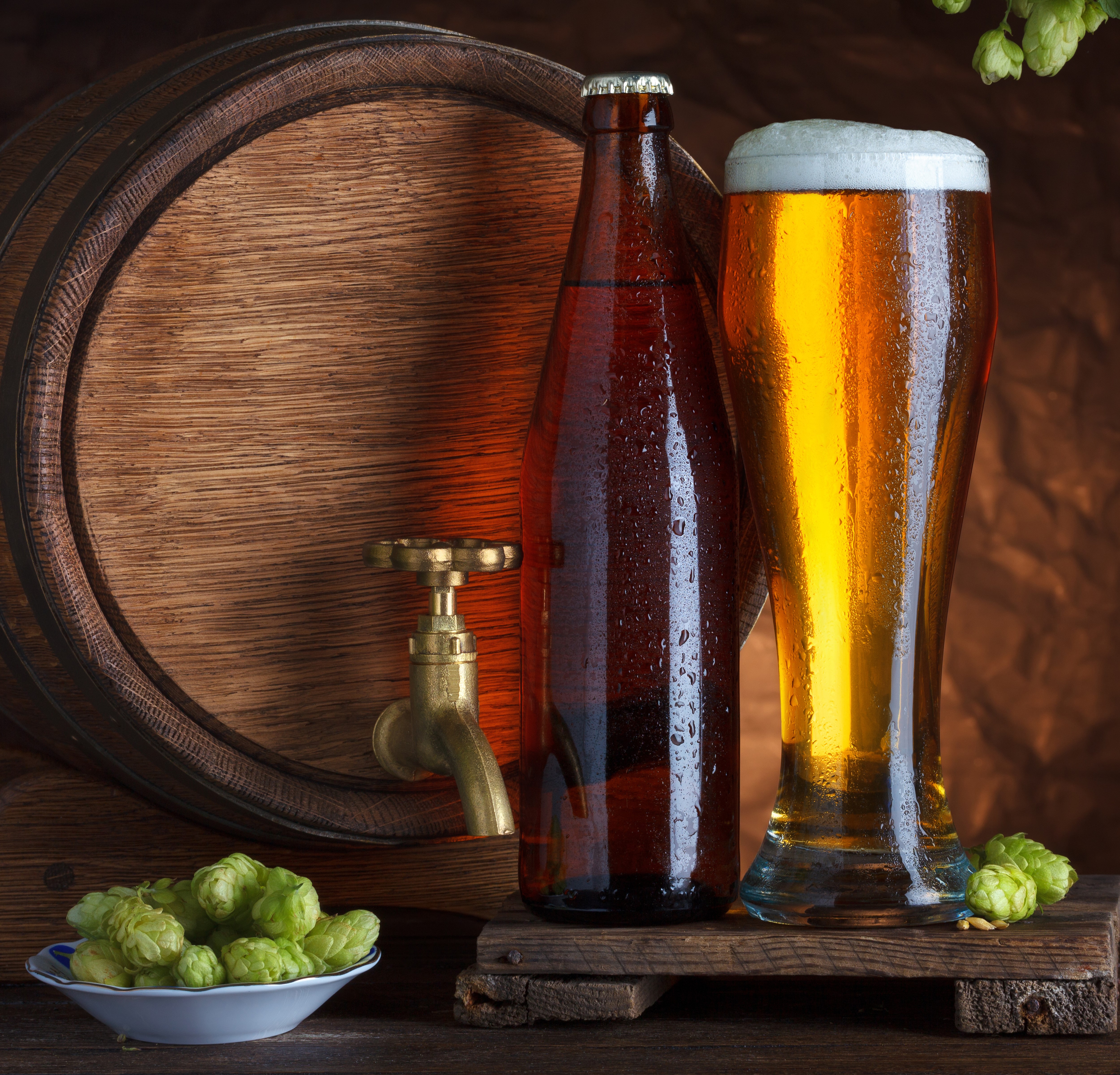 Beer bottle and glass next to a barrel with hops HD Wallpaper