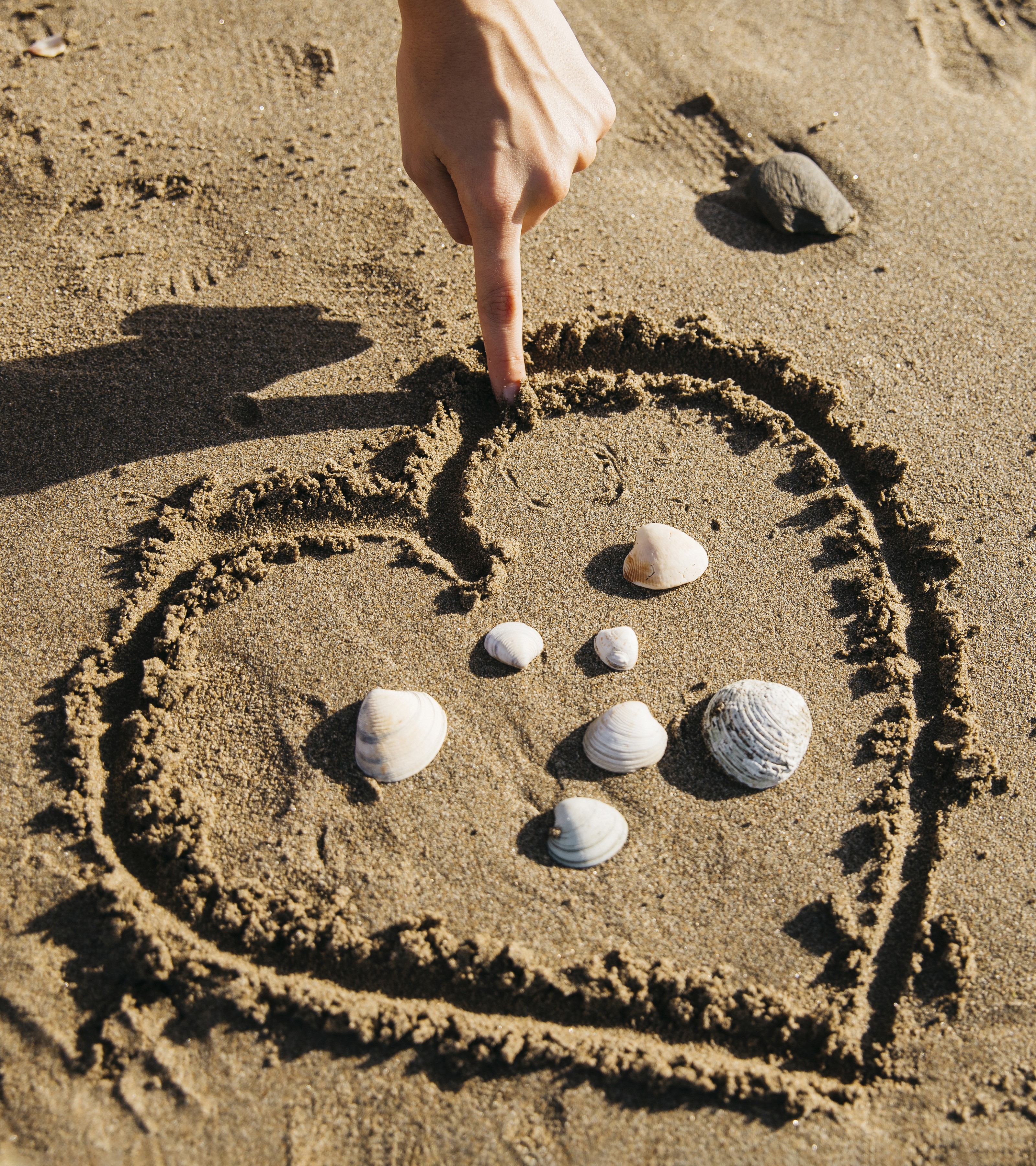 Finger drawing heart in sand with shells HD Wallpaper