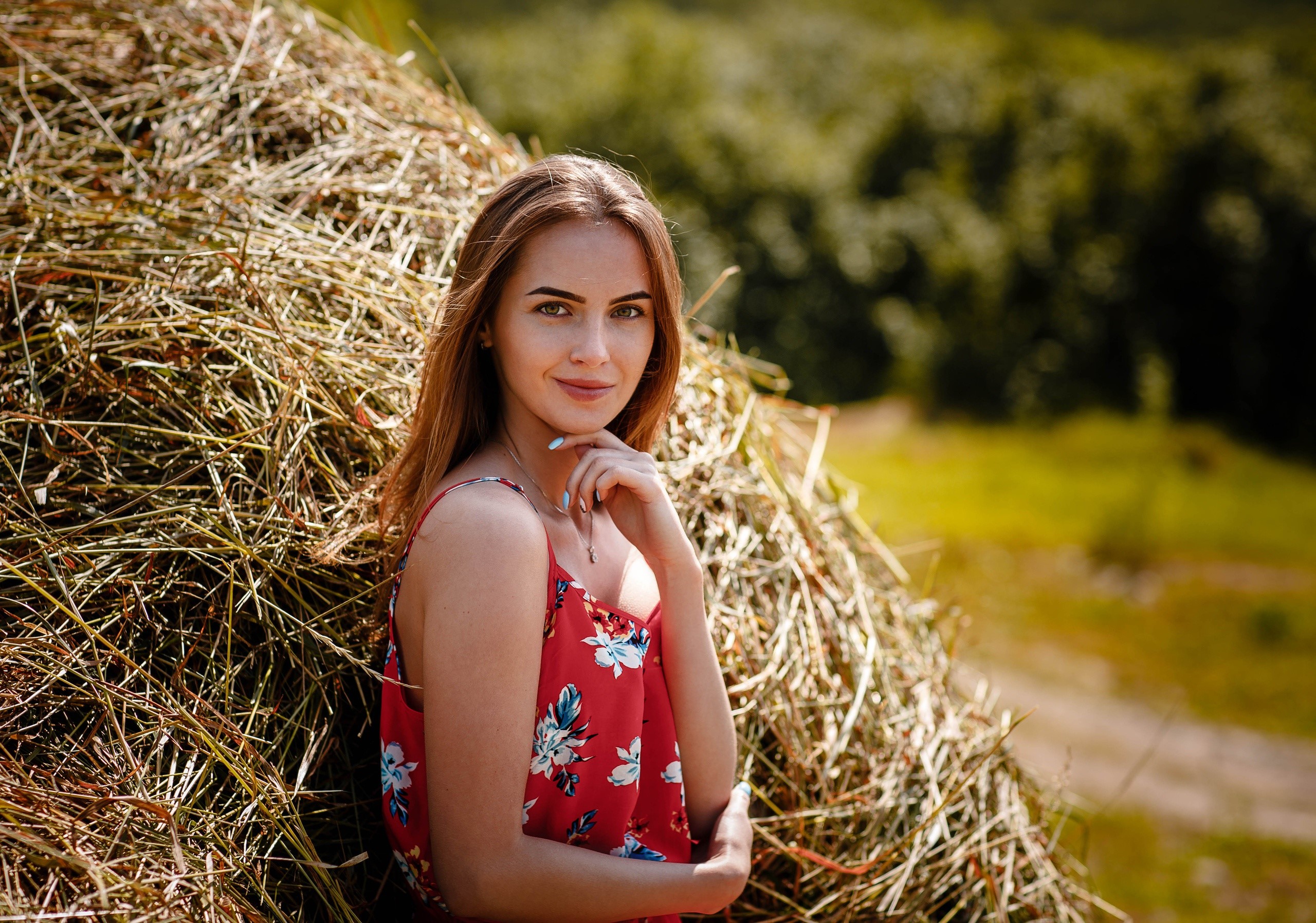 Woman in red floral dress leaning on hay bale HD Wallpaper