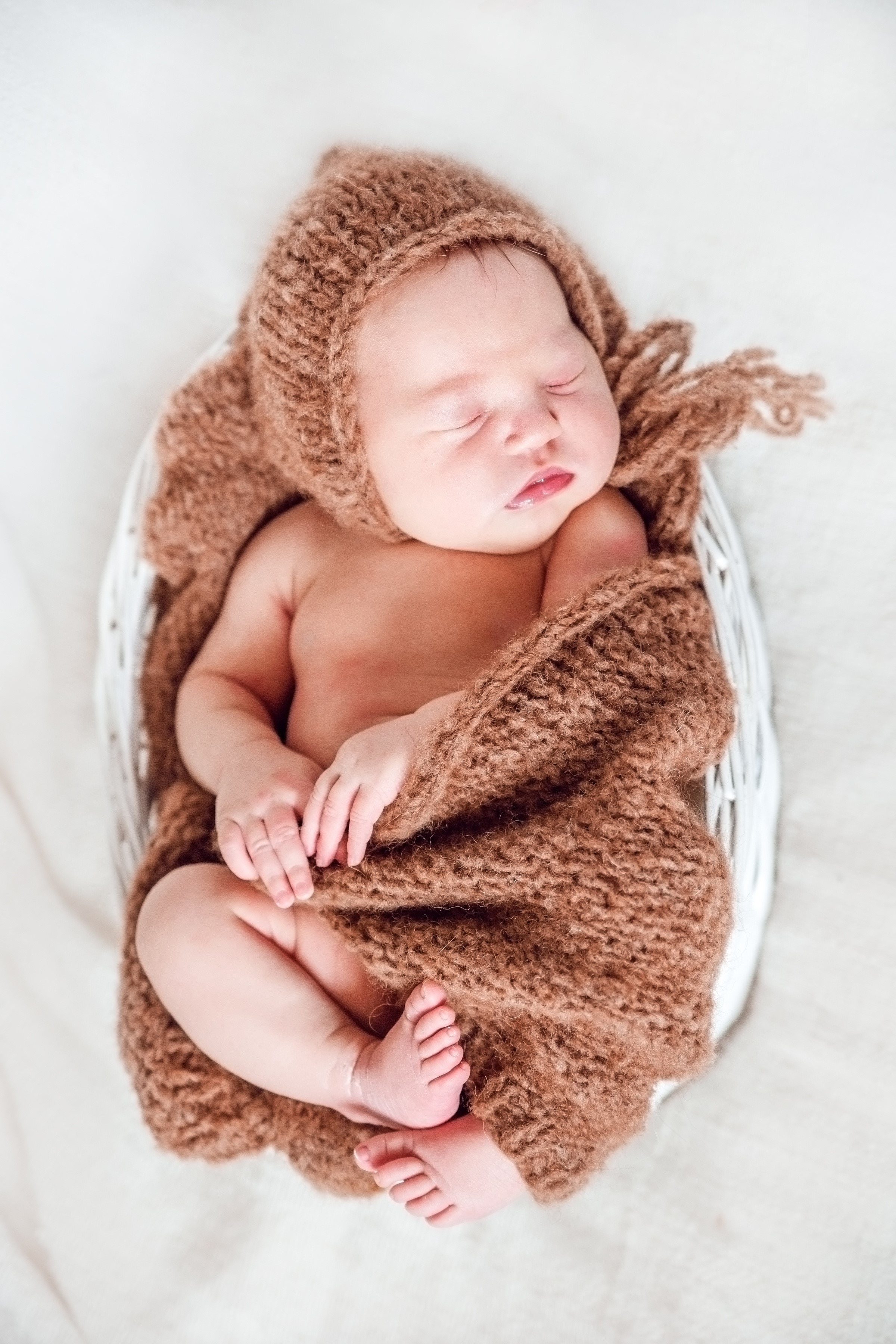 Newborn baby sleeping in a basket with a brown bonnet HD Phone Wallpaper