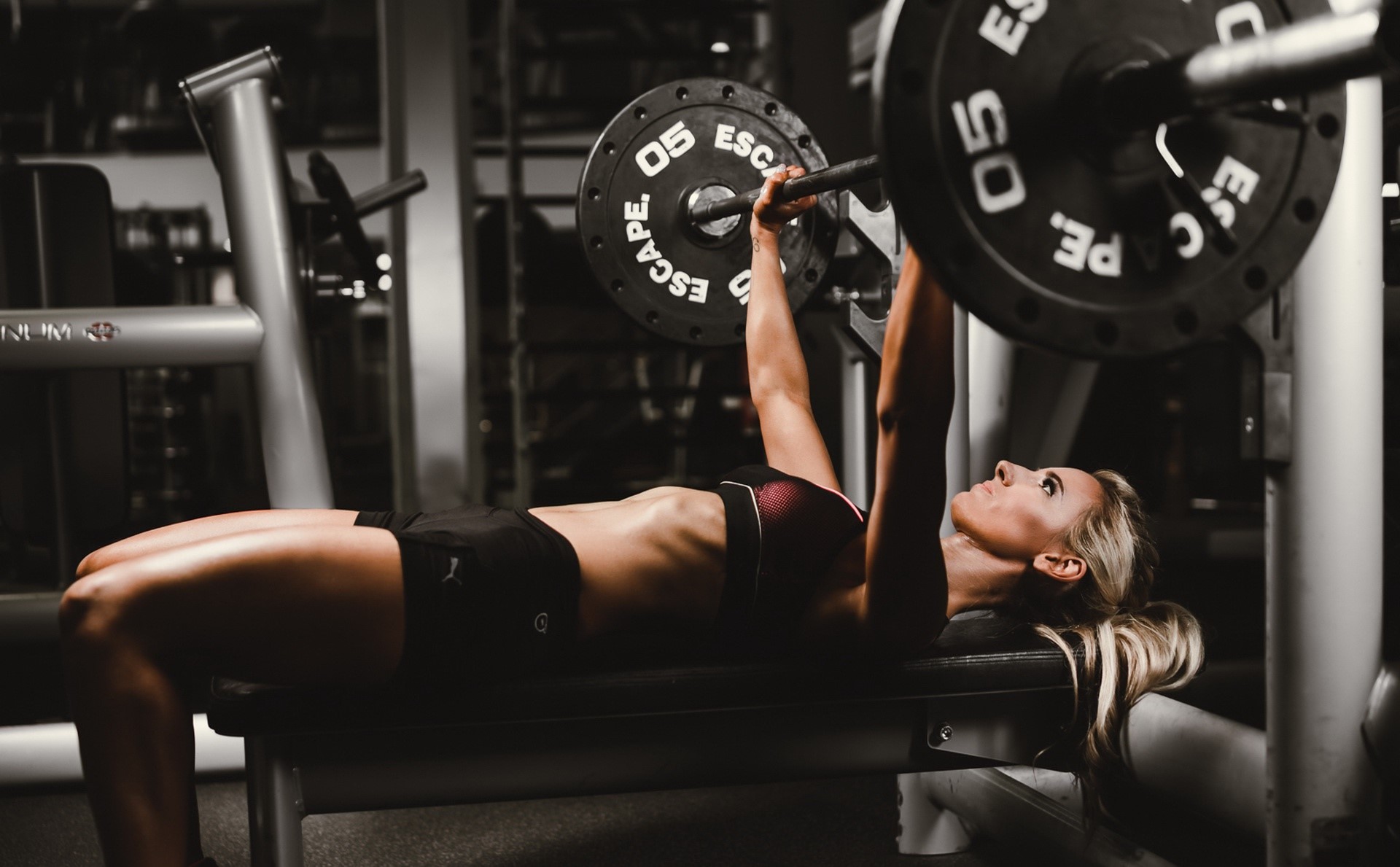 Woman performing bench press with barbell in gym HD Wallpaper