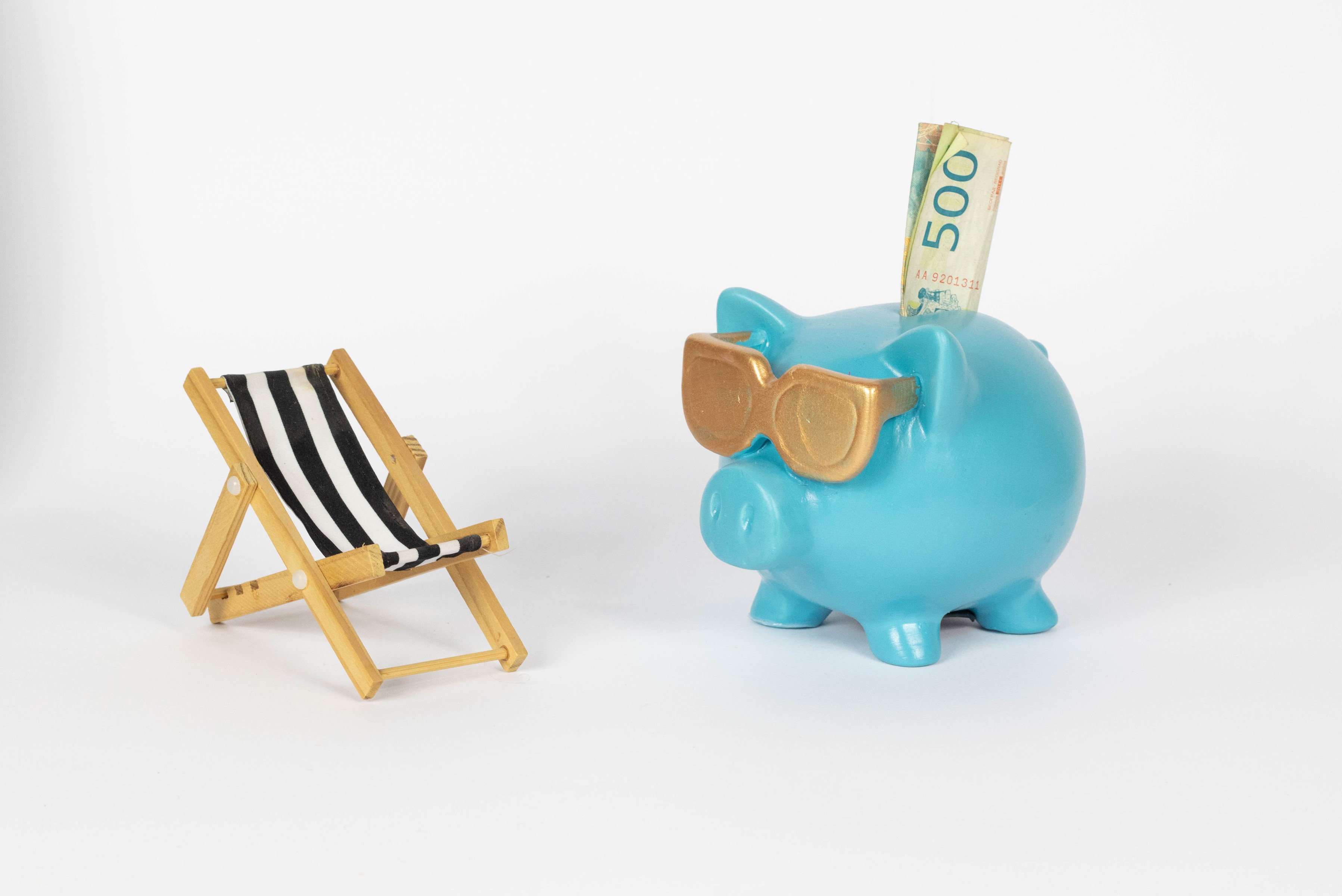 Blue piggy bank with sunglasses and money next to deck chair HD Wallpaper