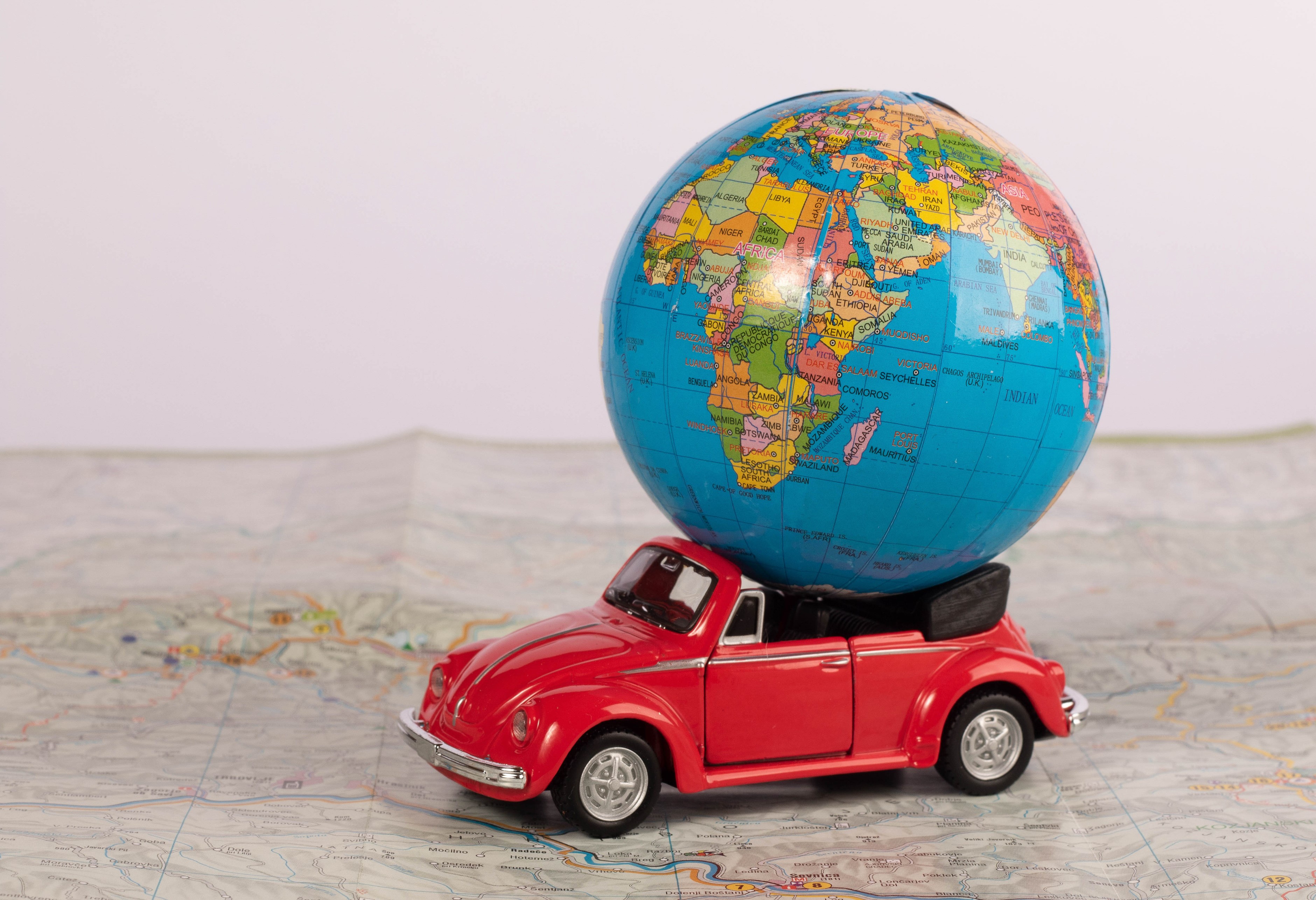 Red toy convertible car carrying a globe on a map HD Wallpaper