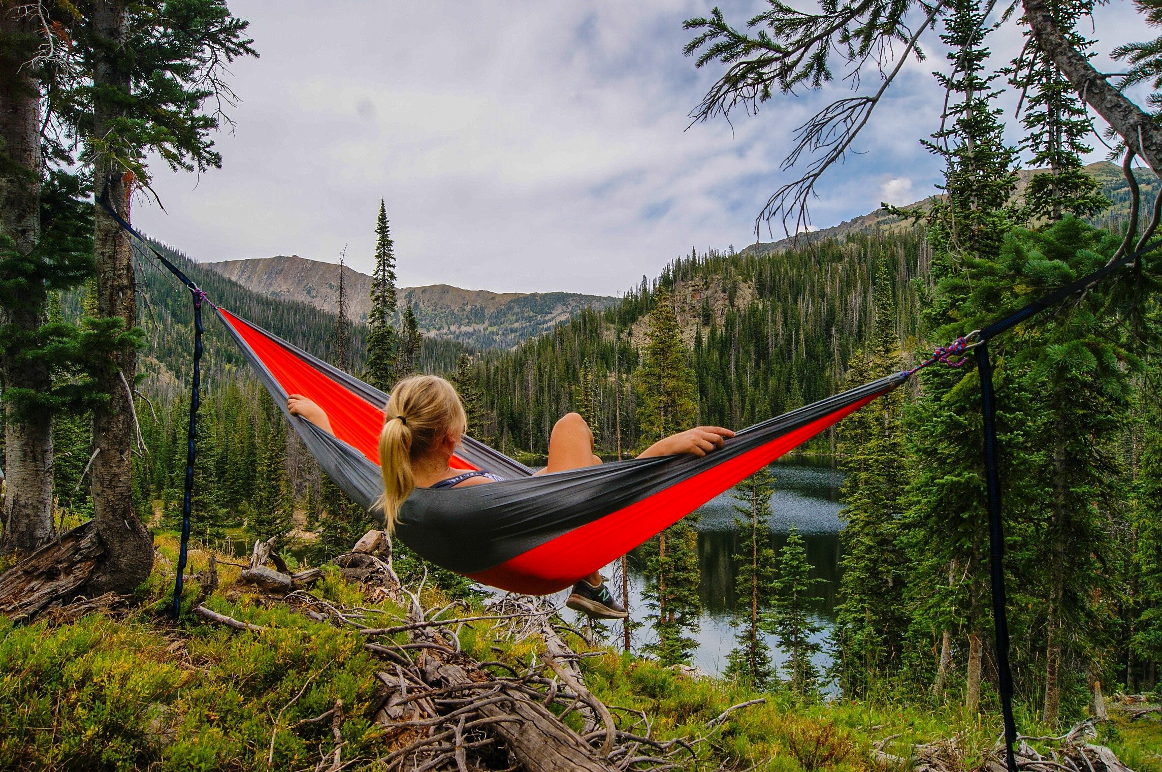 Woman relaxing in a hammock overlooking a mountain lake HD Wallpaper