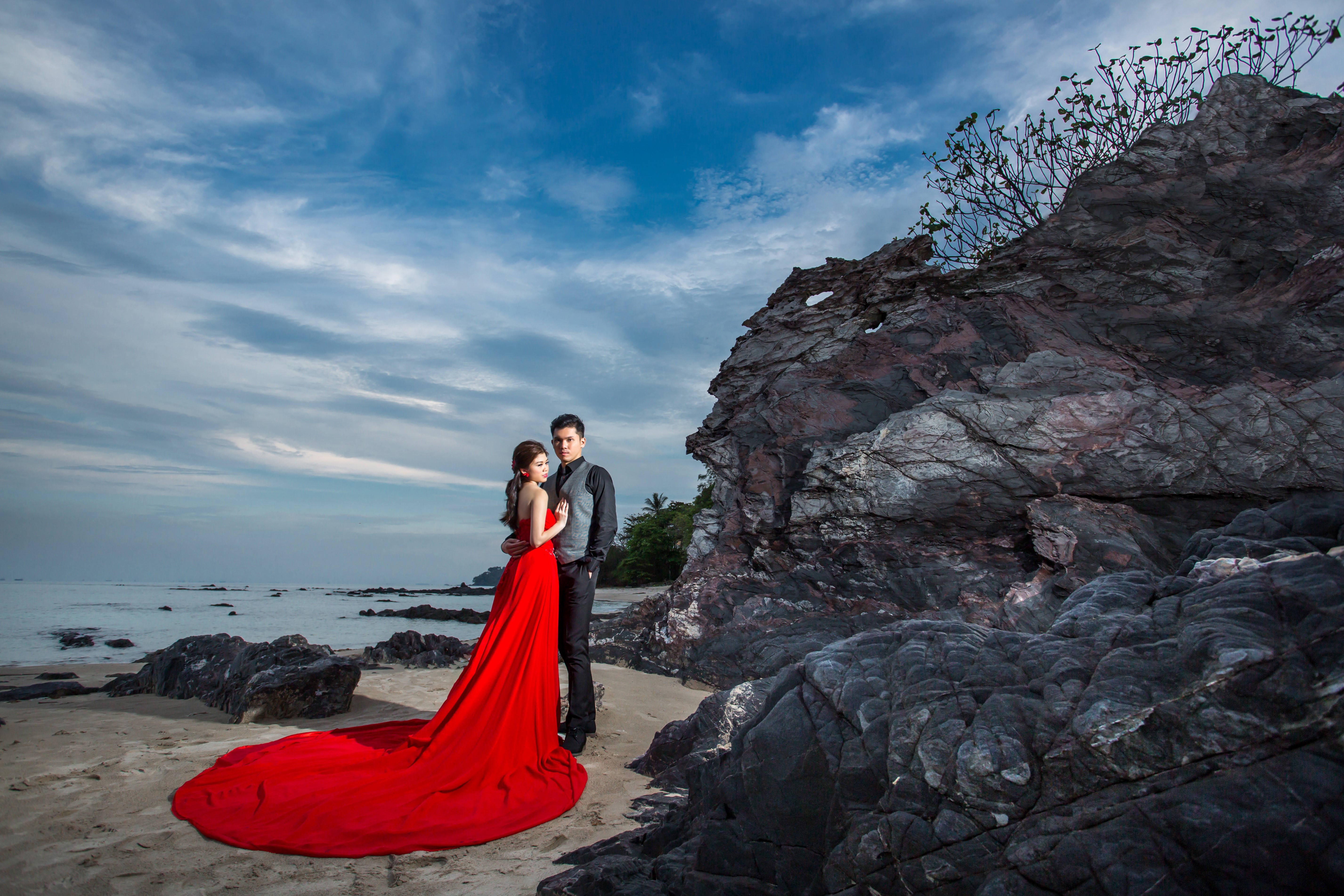 Couple in Red Dress and Suit on Beach with Rocks HD Wallpaper