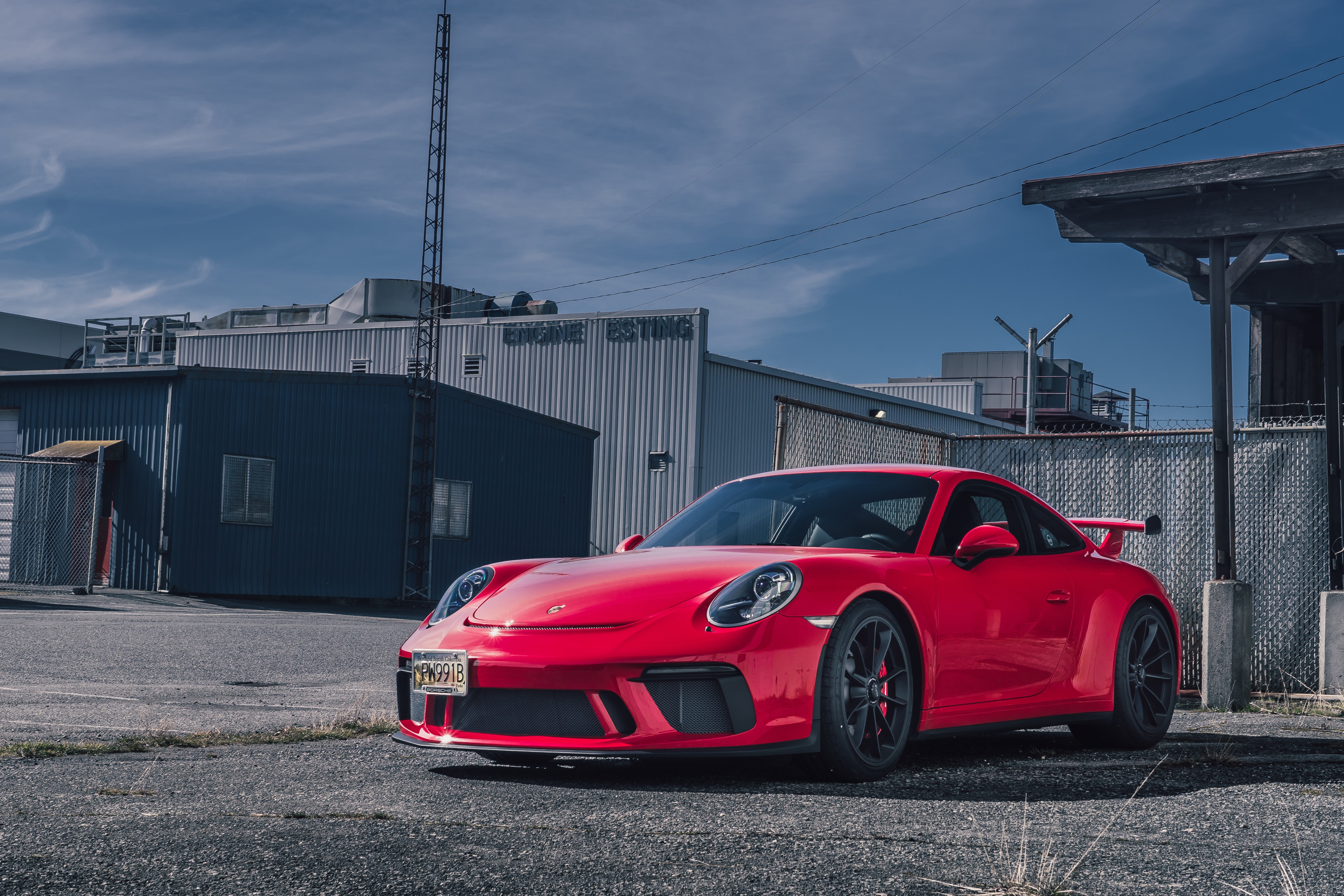 Red Porsche GT3 parked in front of industrial buildings HD Wallpaper