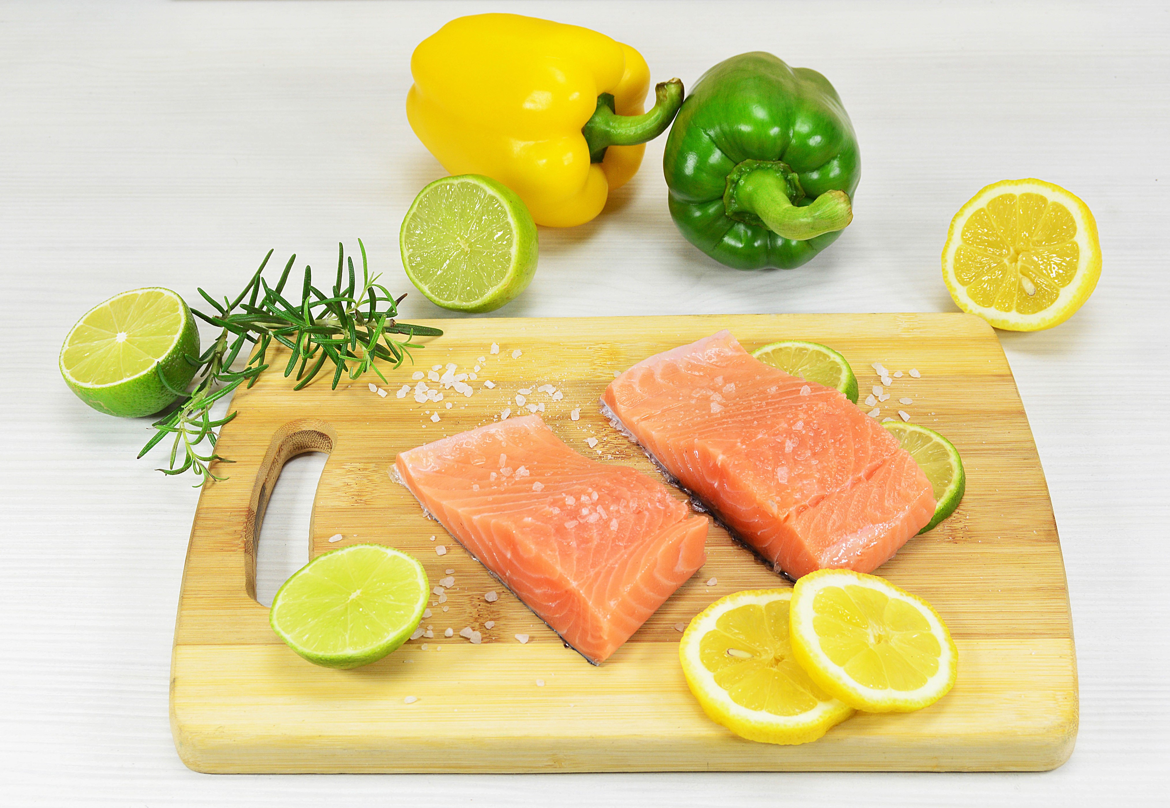 Salmon fillets with limes, lemons, peppers, and rosemary on cutting board HD Wallpaper