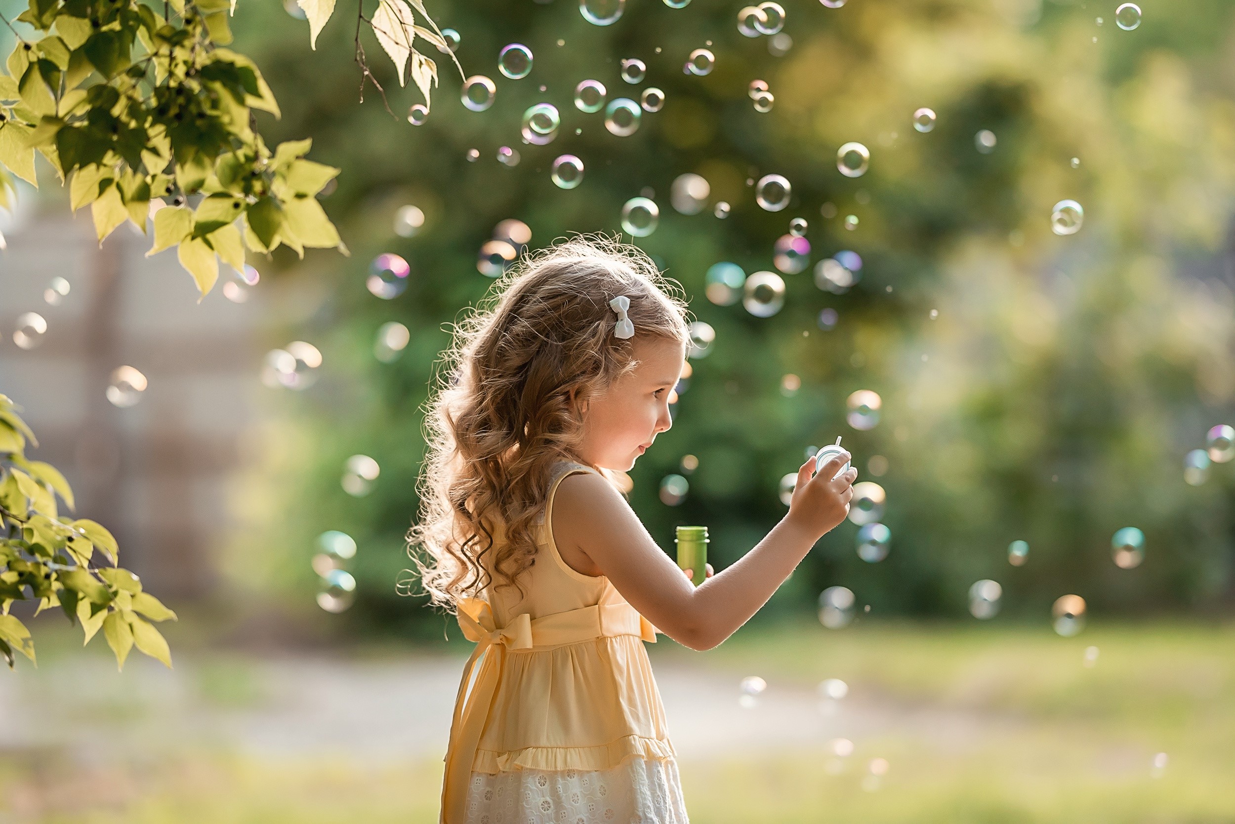 Little girl blowing soap bubbles in a park HD Wallpaper