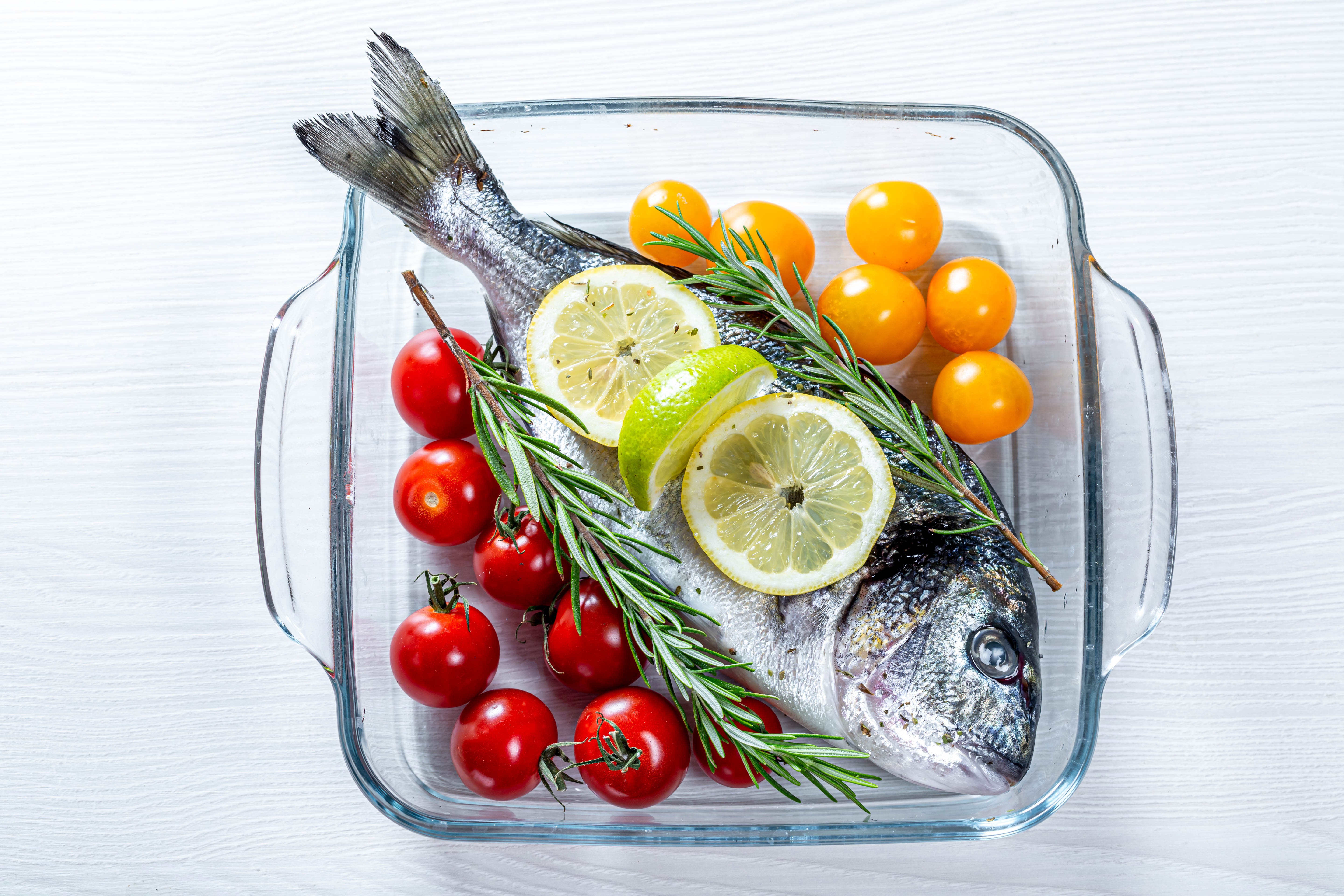 Whole fish with tomatoes, lemon, and rosemary in baking dish HD Wallpaper